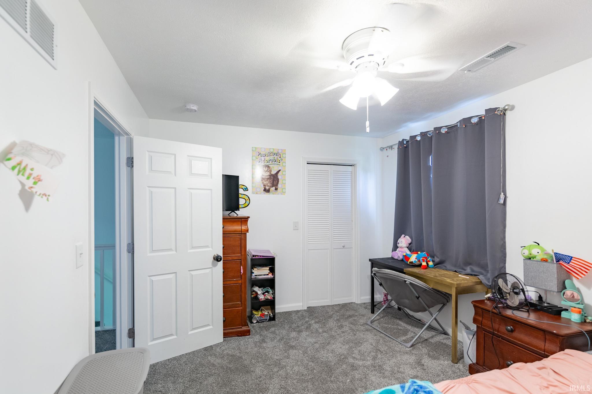 Carpeted room featuring a white paneled door, bi-fold closet doors, a ceiling fan, and a window with dark curtains