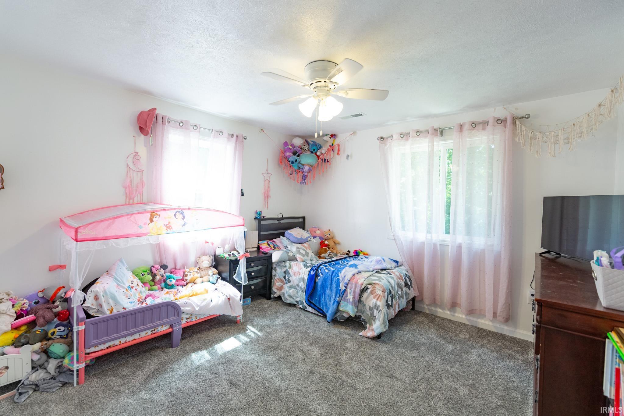 Carpeted room featuring multiple windows, a ceiling fan with integrated lighting, and white painted walls