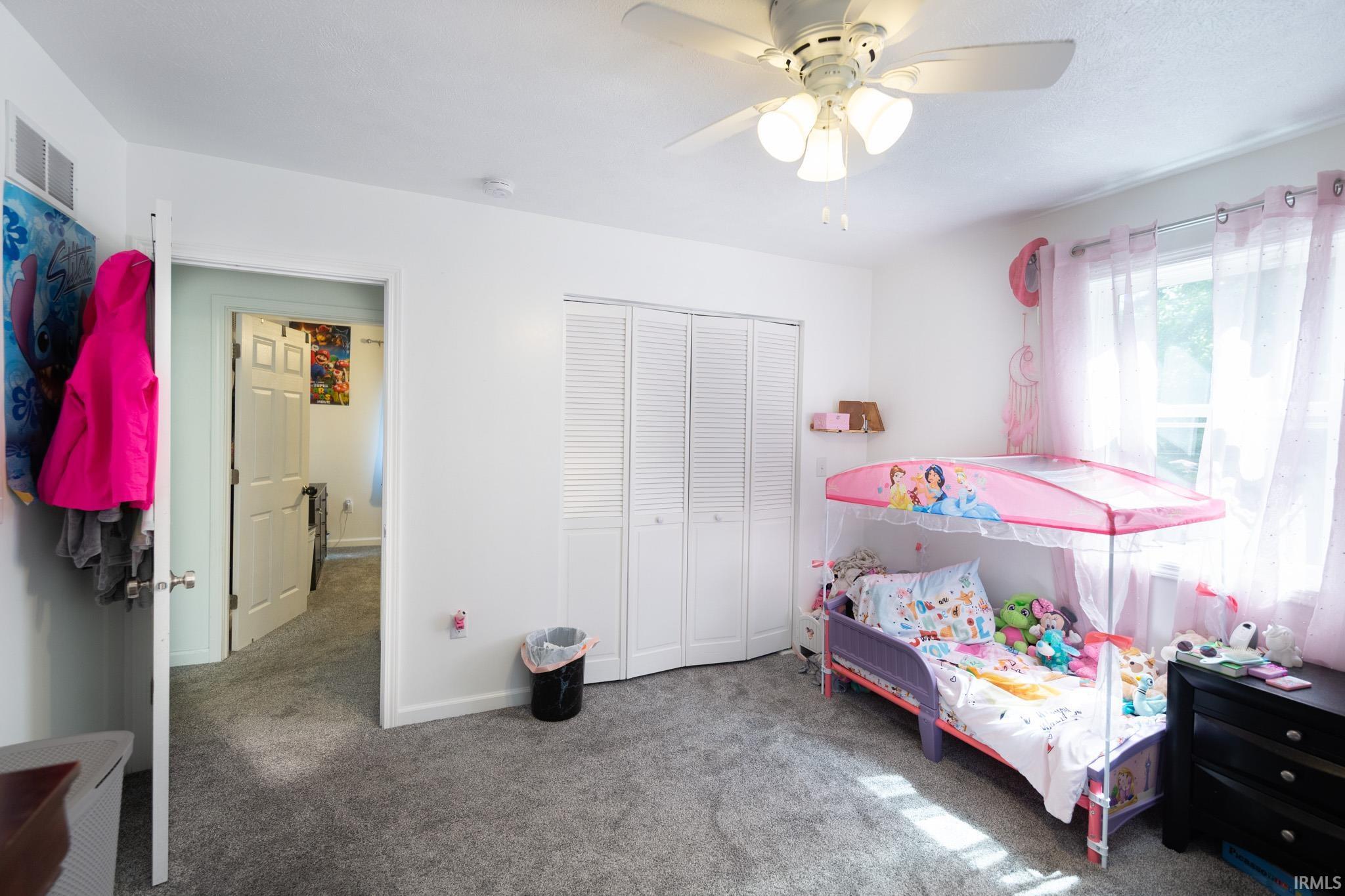 Bedroom featuring a ceiling fan with light fixture, gray carpet flooring, white louvered bifold closet doors, and white walls
