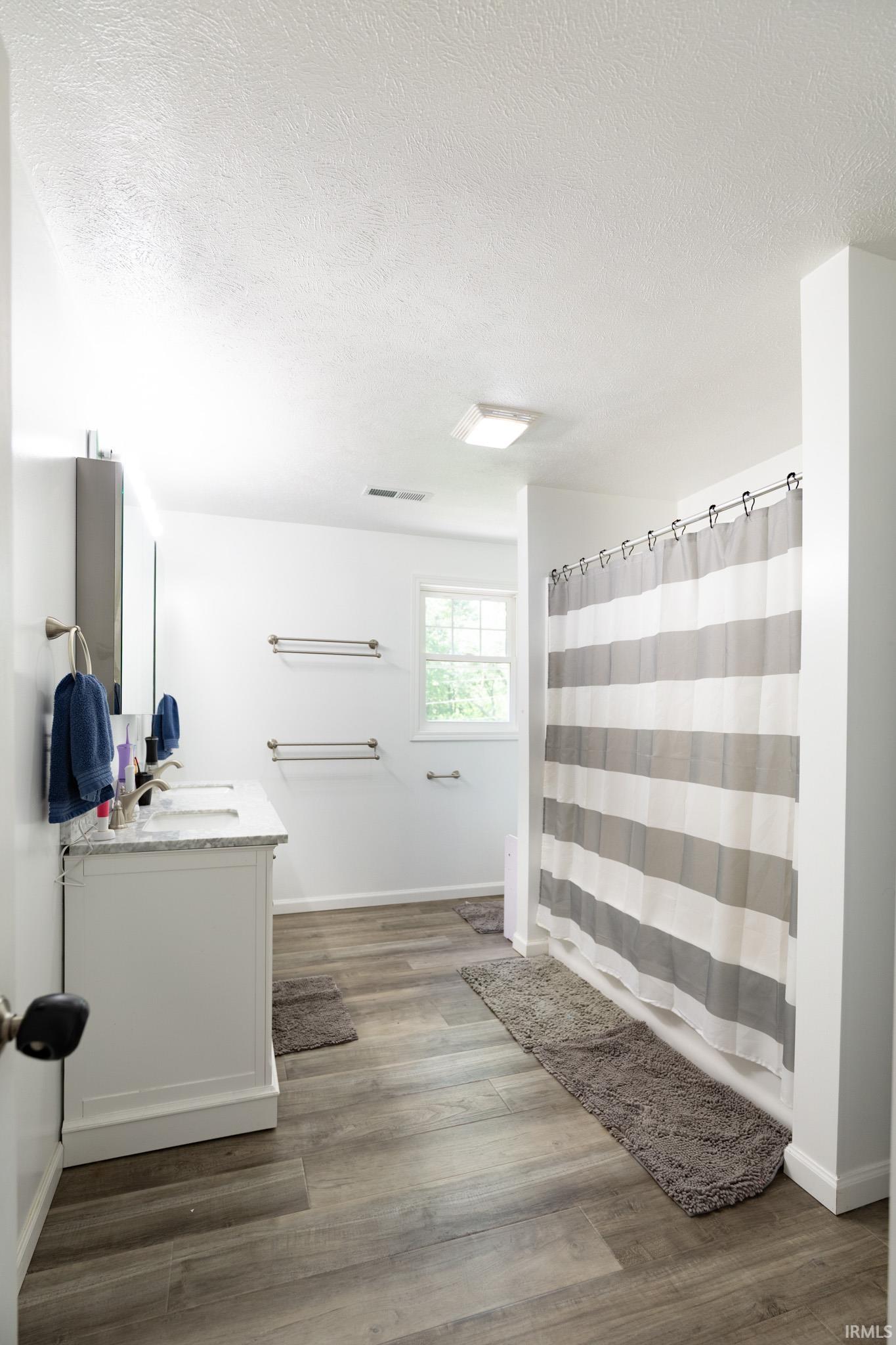 Bathroom featuring a double vanity with stone countertop, dual undermount sinks, and wood-finish flooring