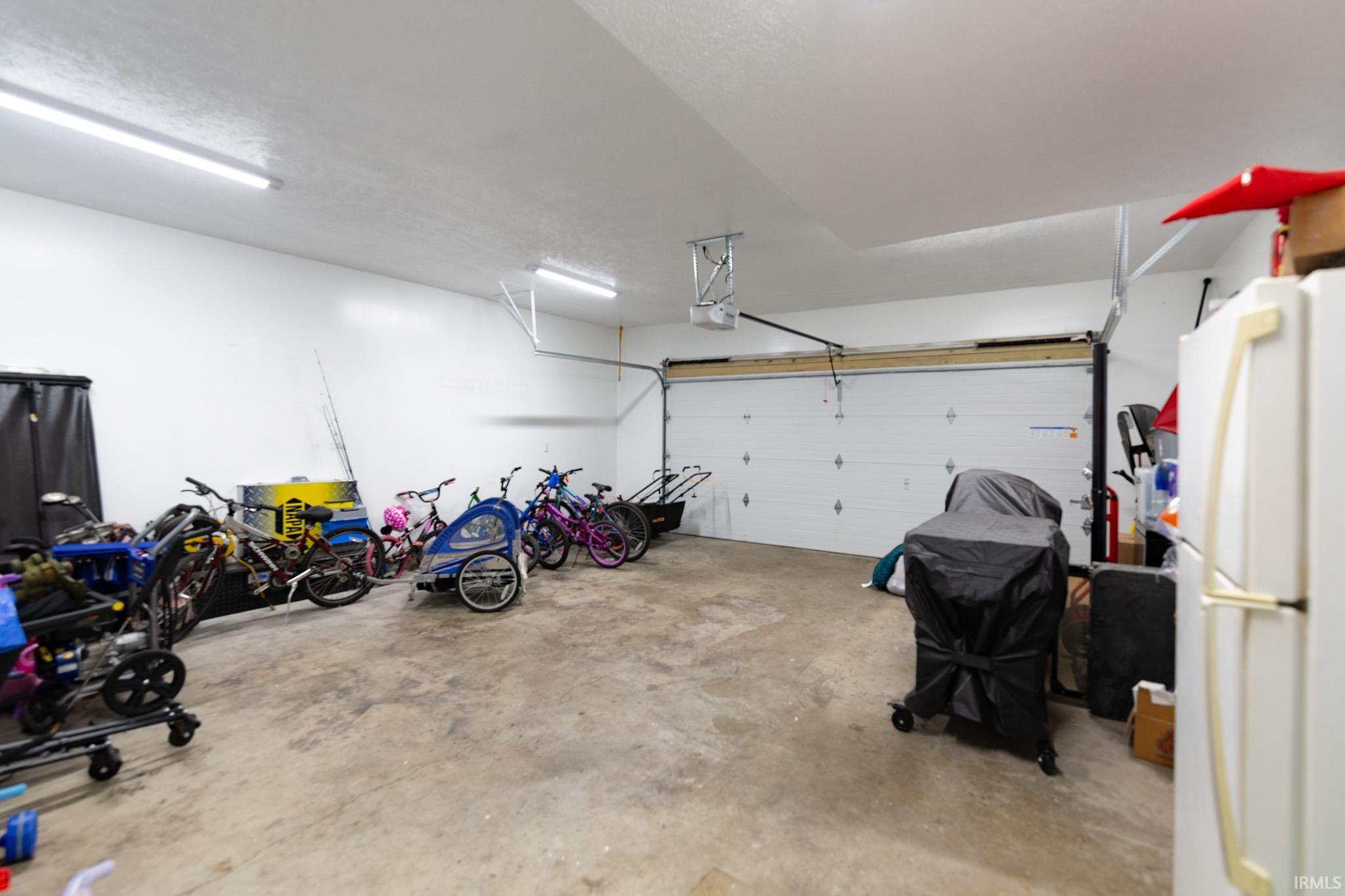 Spacious garage featuring a concrete floor, bright white walls, overhead fluorescent lighting, and an automatic garage door opener