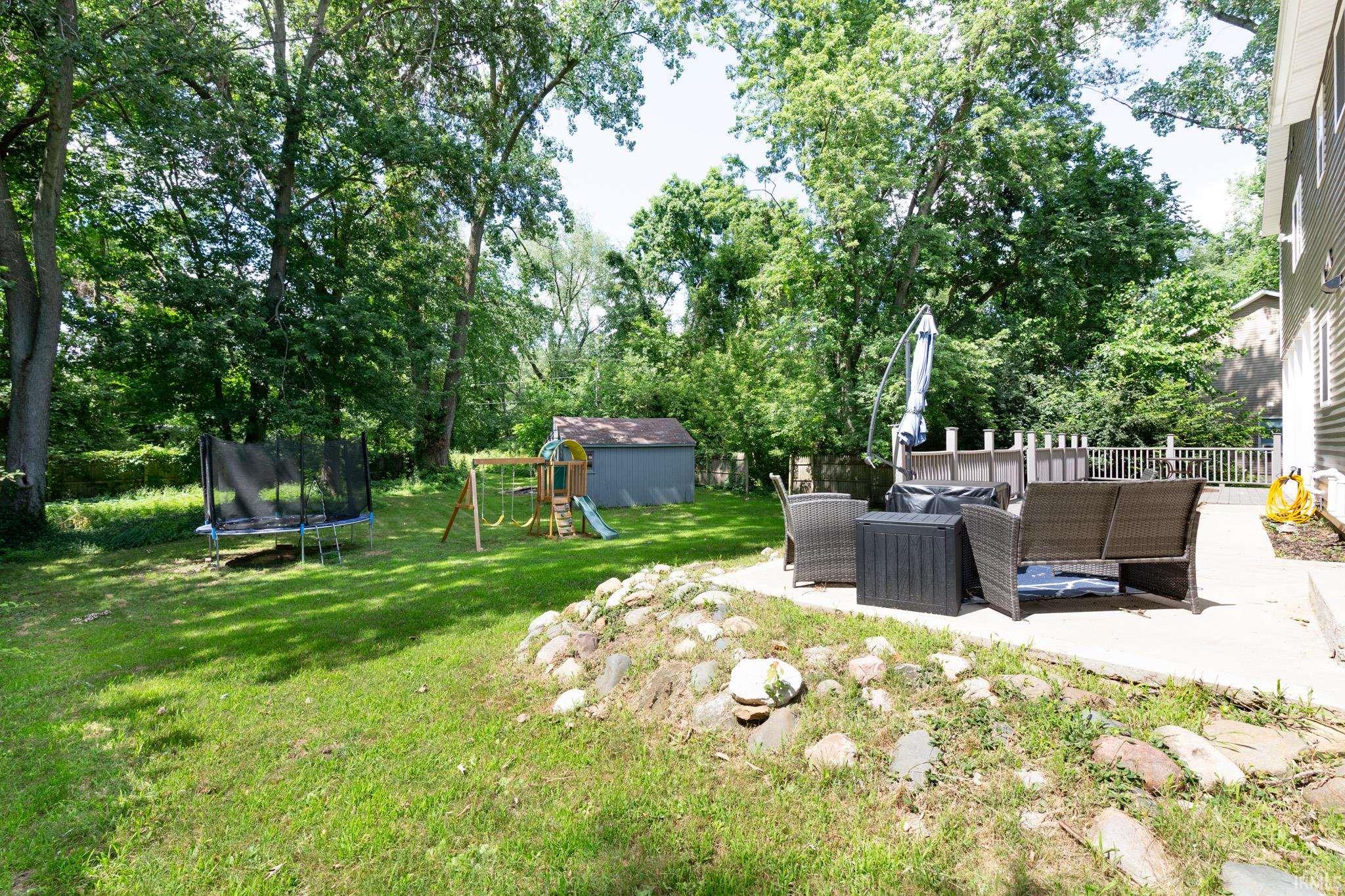Spacious backyard featuring a concrete patio, a privacy fence, and mature trees providing natural shading