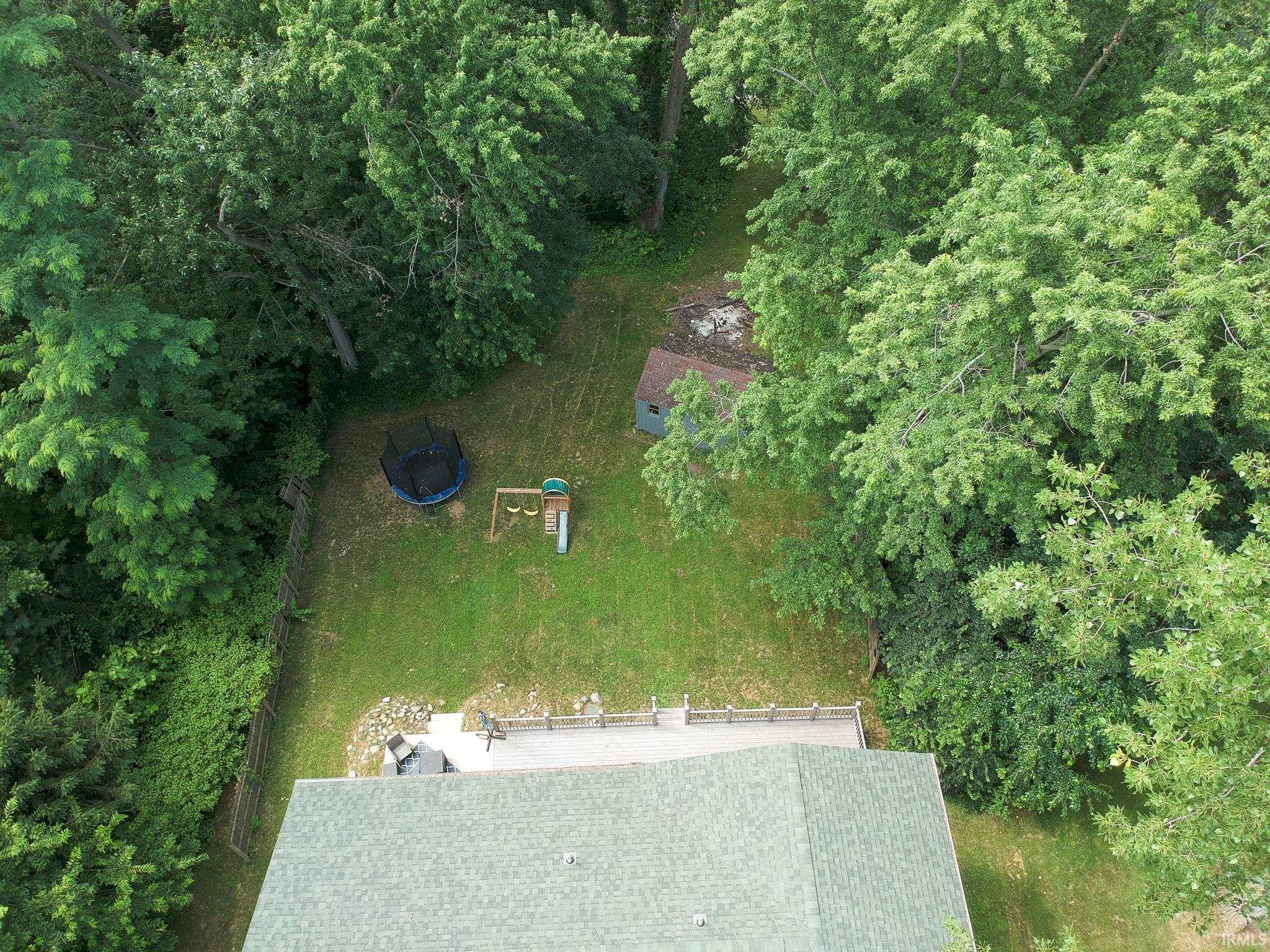 Expansive backyard featuring a green lawn, wood fence, and mature trees