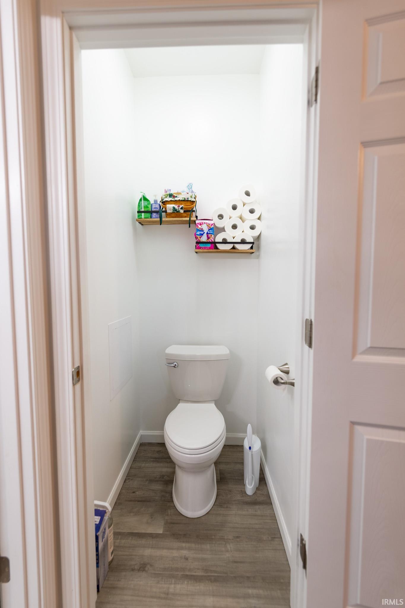 Powder room featuring a single toilet, wood-finish flooring, and white baseboards