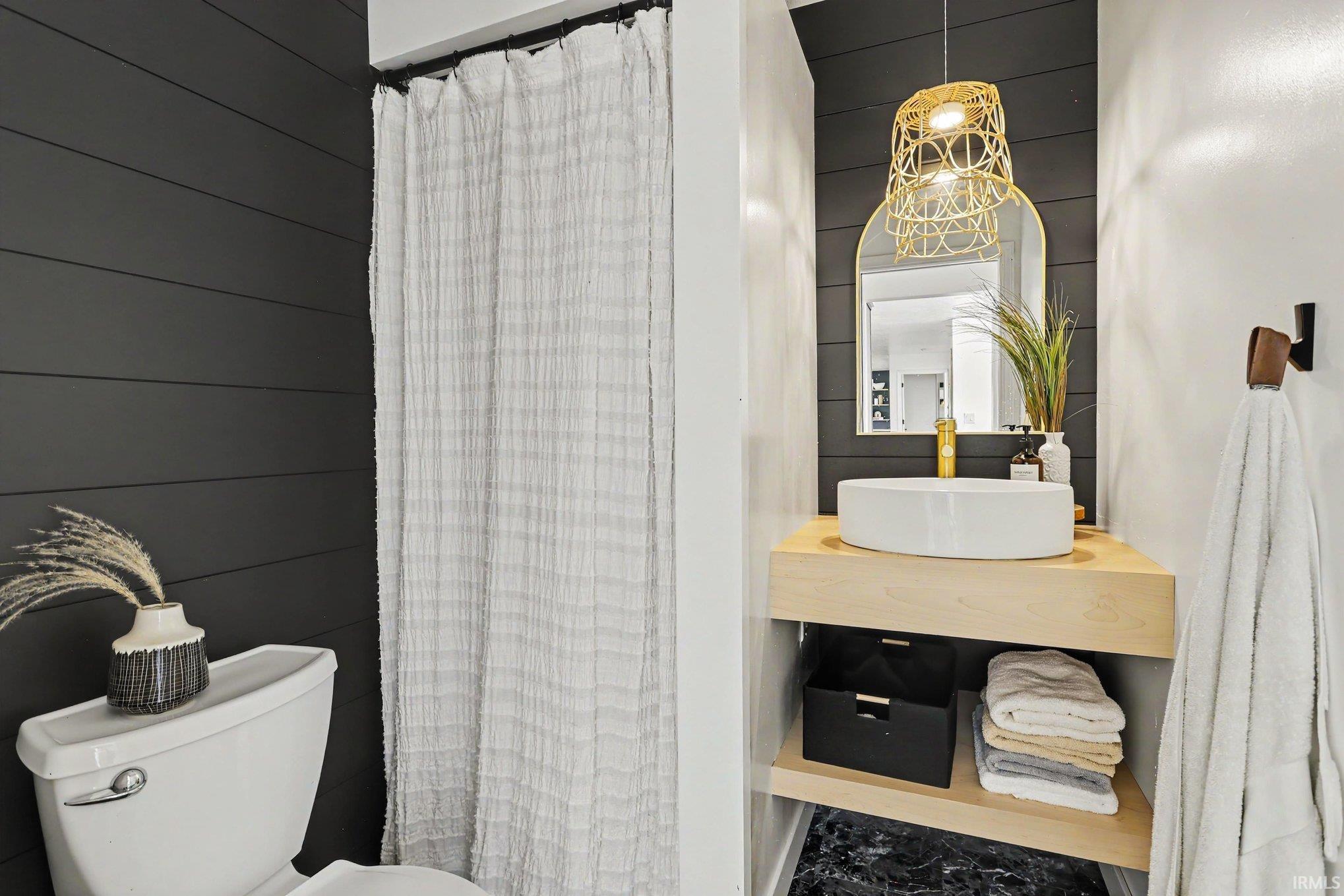 Floating wood-finish vanity with a vessel sink and gold-tone faucet, complemented by a contemporary rattan pendant light