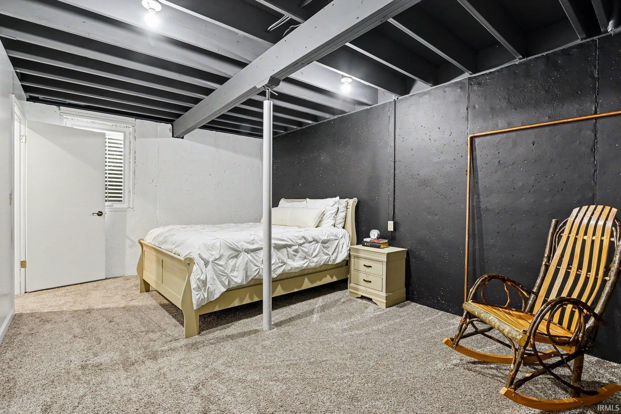 Finished lower level space featuring exposed ceiling joists, light-colored carpeting, white interior door, and a horizontal window with white blinds