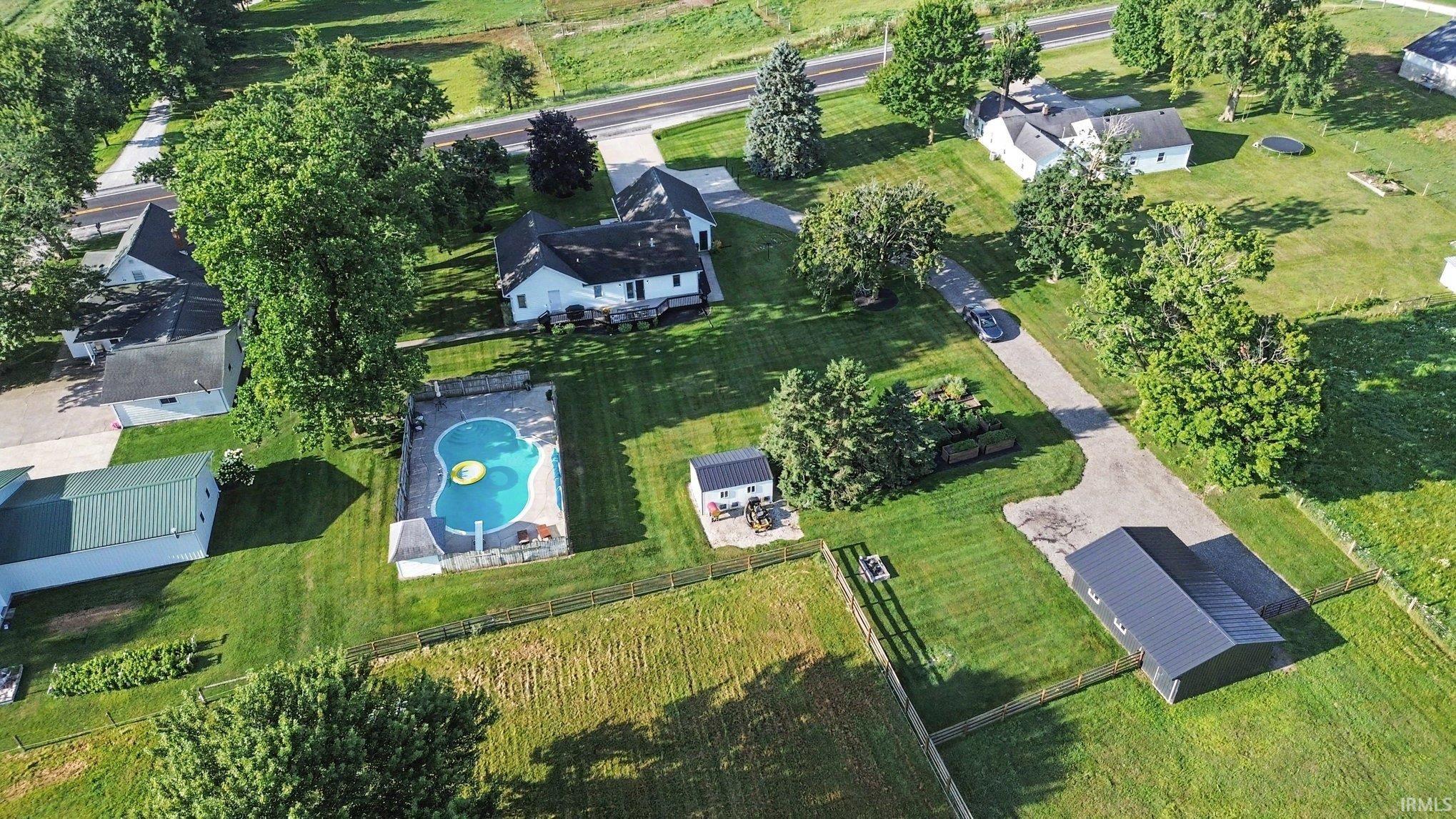 Expansive property featuring a main residence, fenced in-ground pool with surrounding patio, detached outbuilding, secondary outbuilding, and mature trees
