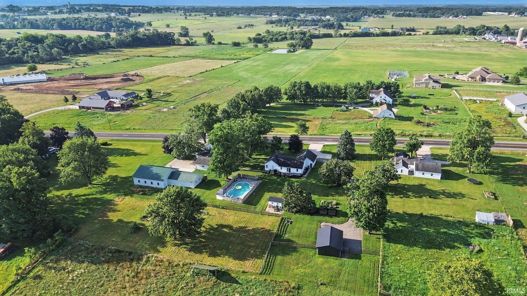 Expansive property featuring multiple structures, a swimming pool, mature trees, and open green spaces