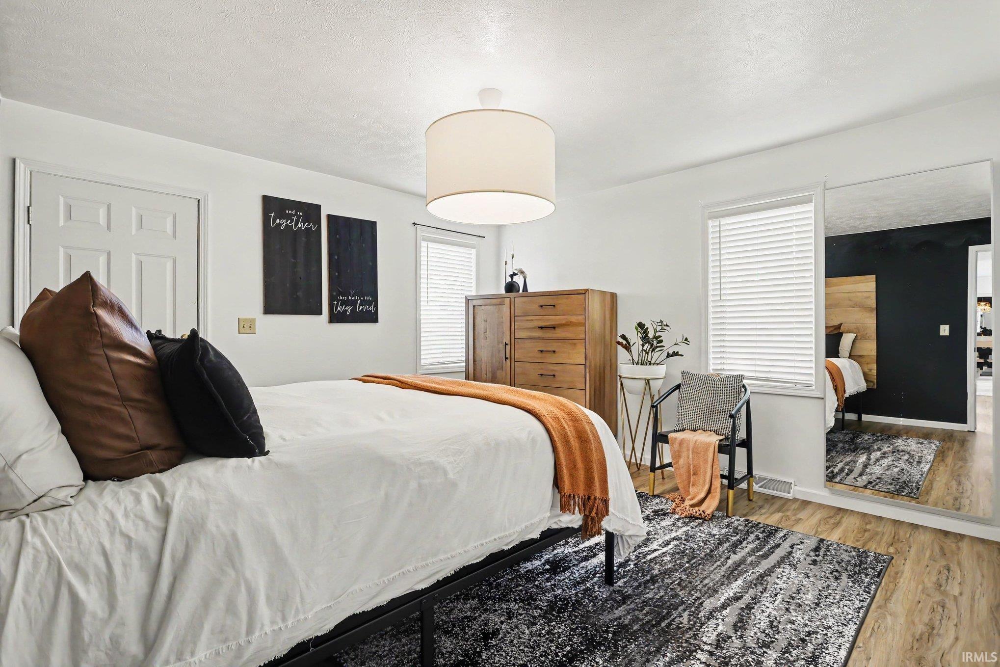 Bedroom featuring light wood-finish flooring, white walls, and a large drum pendant light fixture