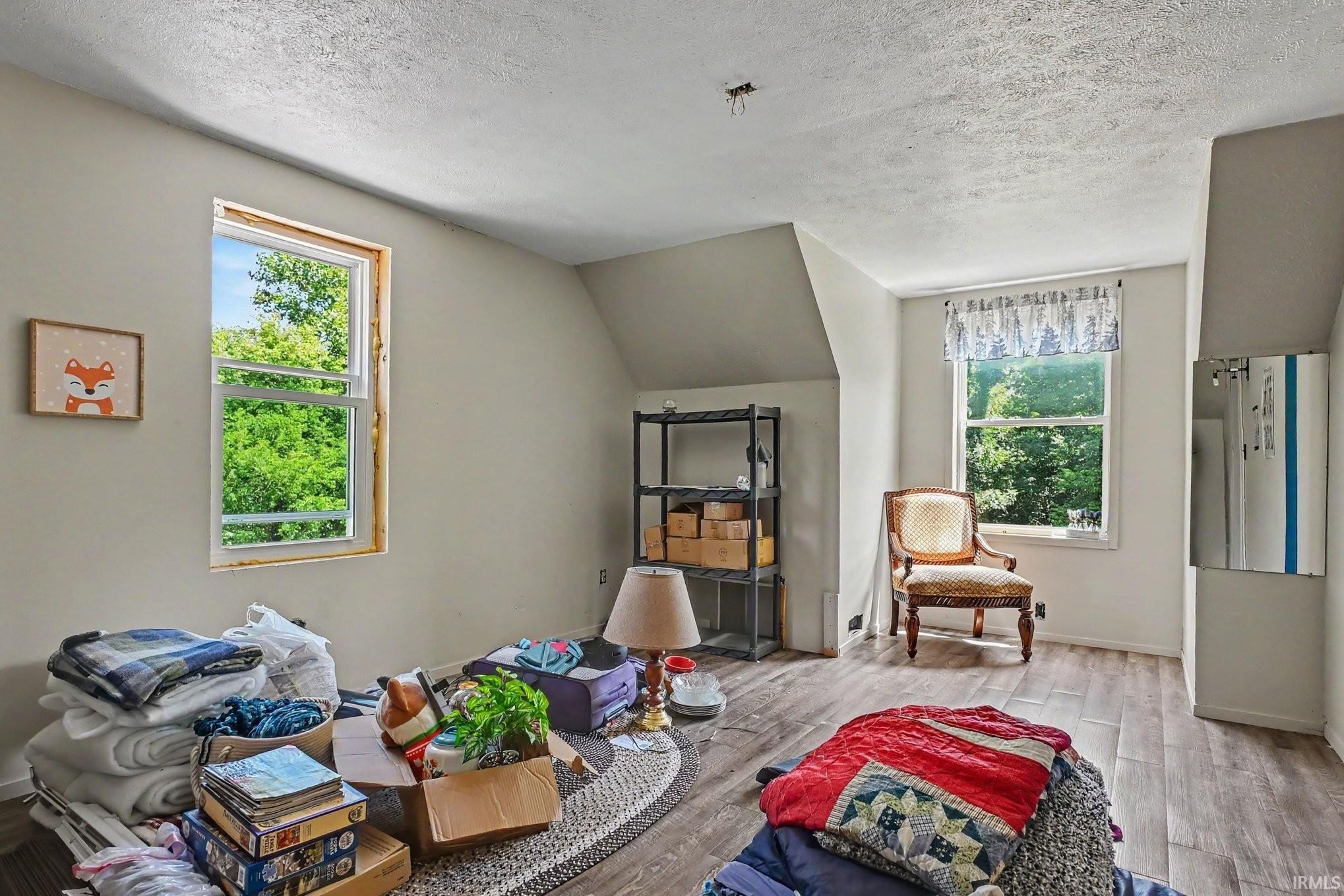 Room featuring sloped ceilings, two double-hung windows with exterior landscaping, and wood-finish flooring