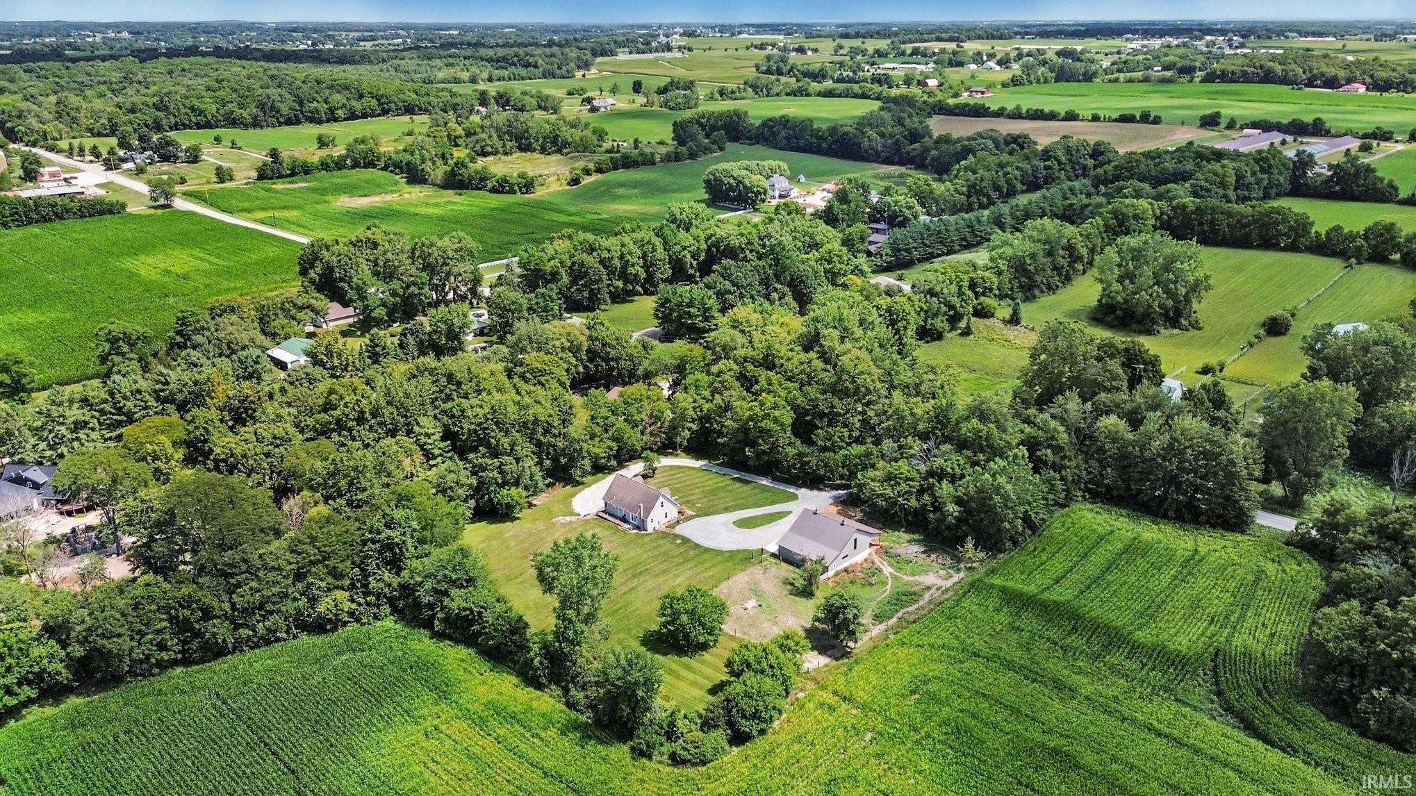 Expansive aerial perspective showcasing two properties amidst verdant fields and mature trees