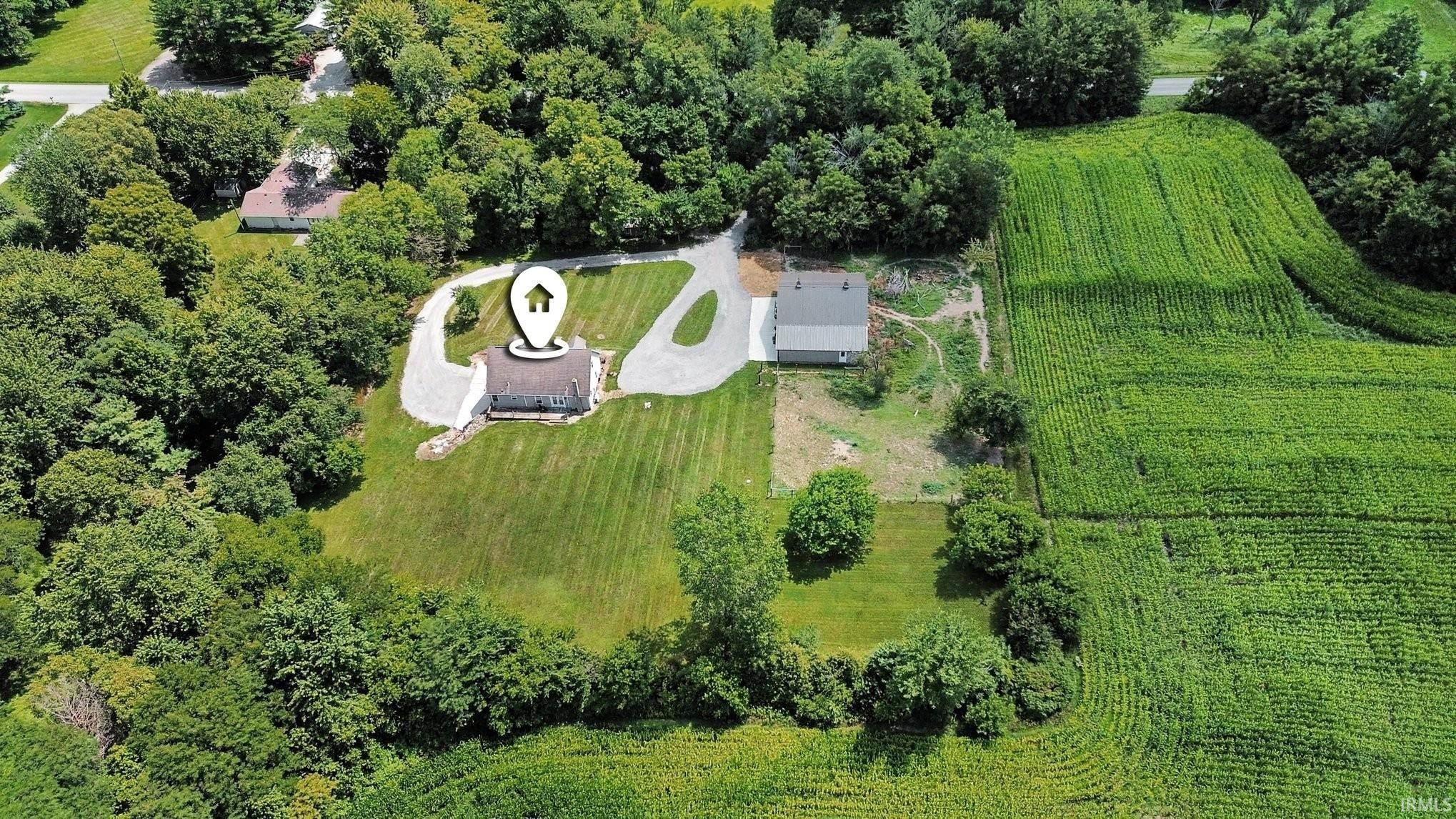 Aerial perspective showcasing a property with a gravel driveway, surrounded by mature trees and verdant lawns