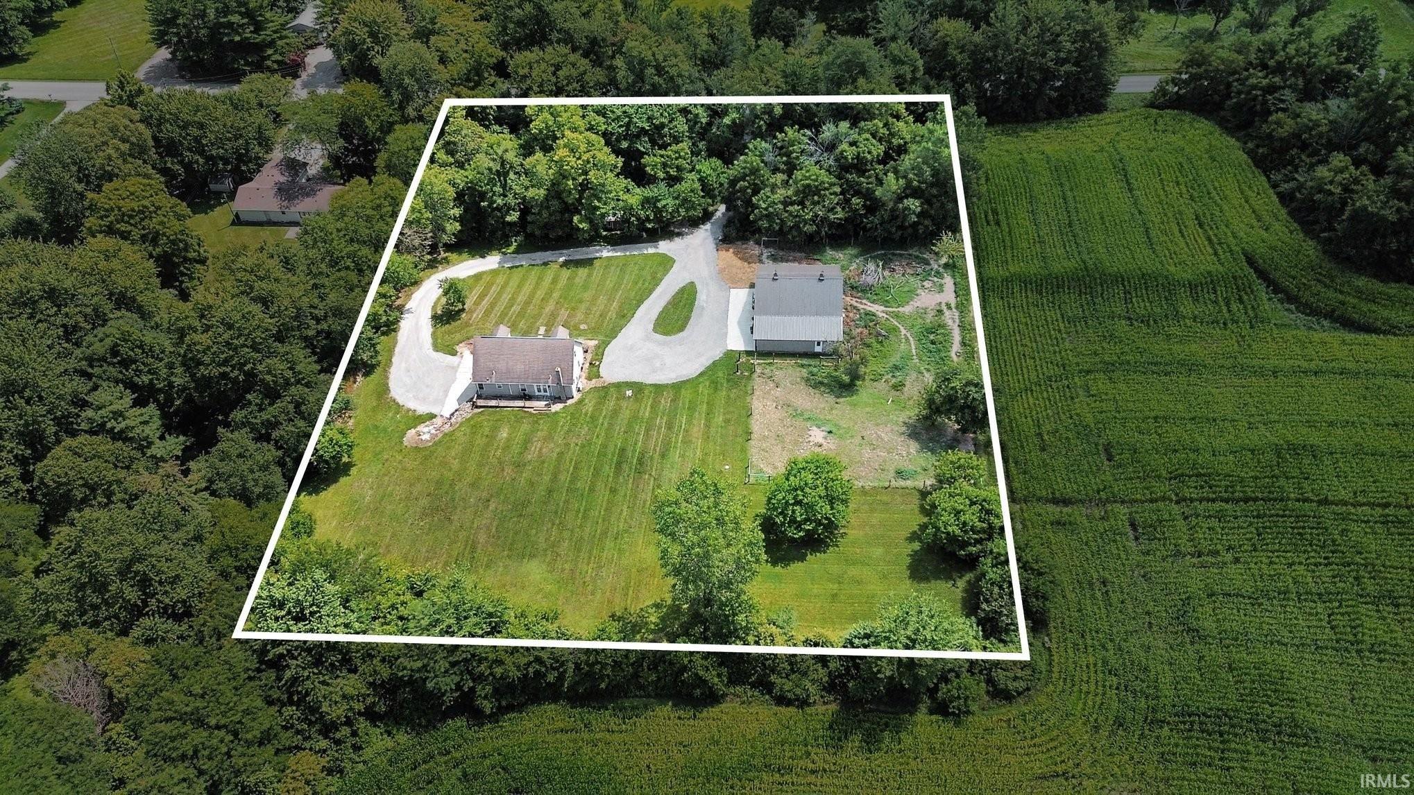 Expansive property featuring two distinct structures, a gravel driveway, mature trees, and a substantial grassy area