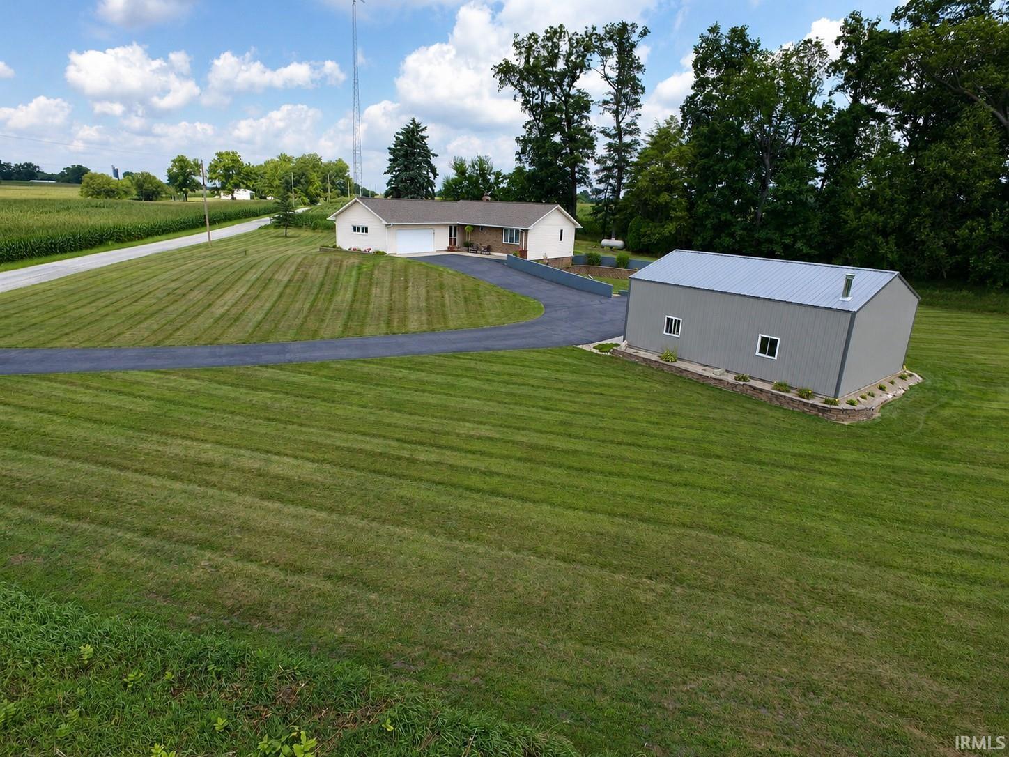 Expansive green lawn with a long asphalt driveway, a detached metal-sided outbuilding with a metal roof, and surrounding mature trees