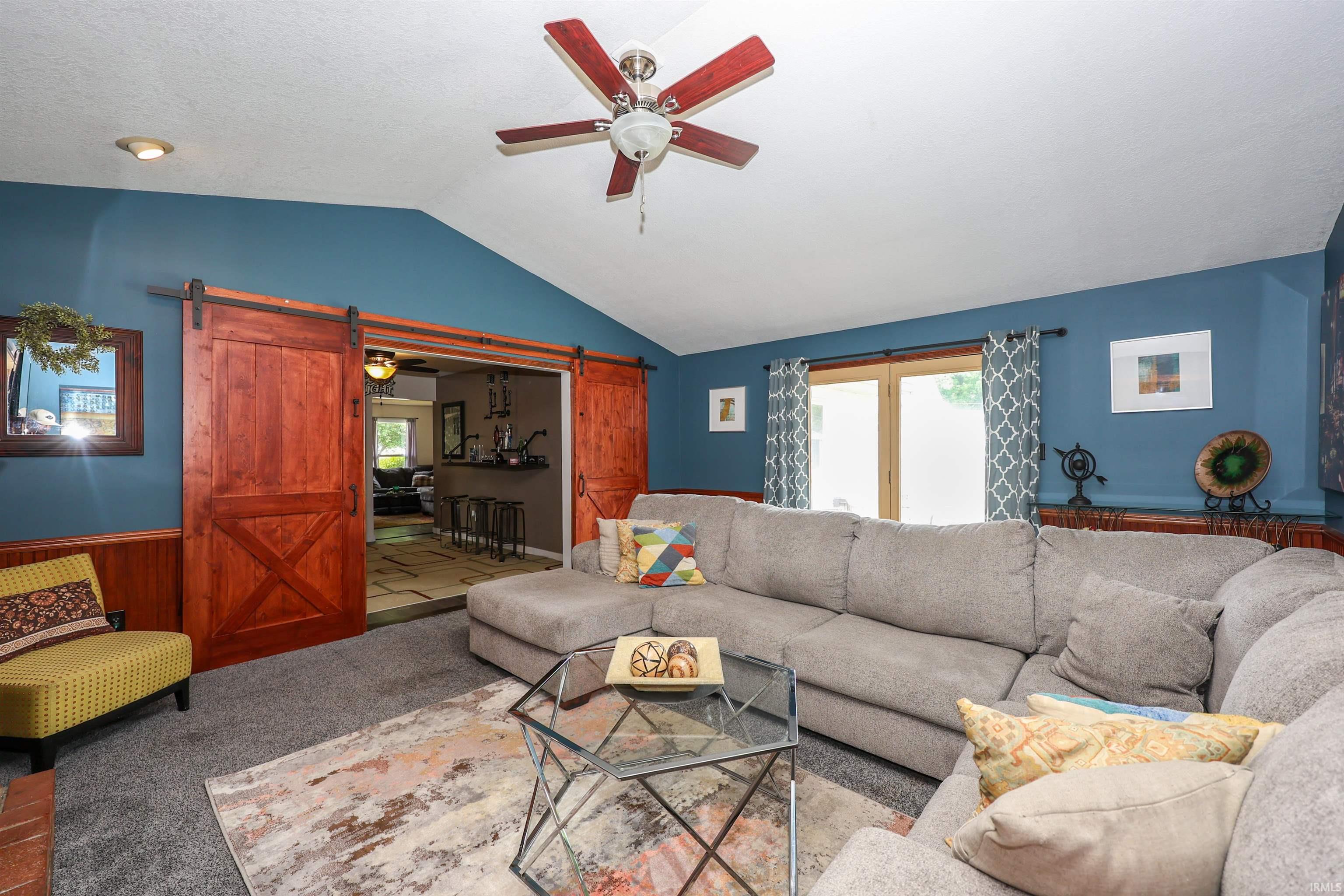 Living area featuring vaulted ceilings, a ceiling fan, and wood-paneled wainscoting