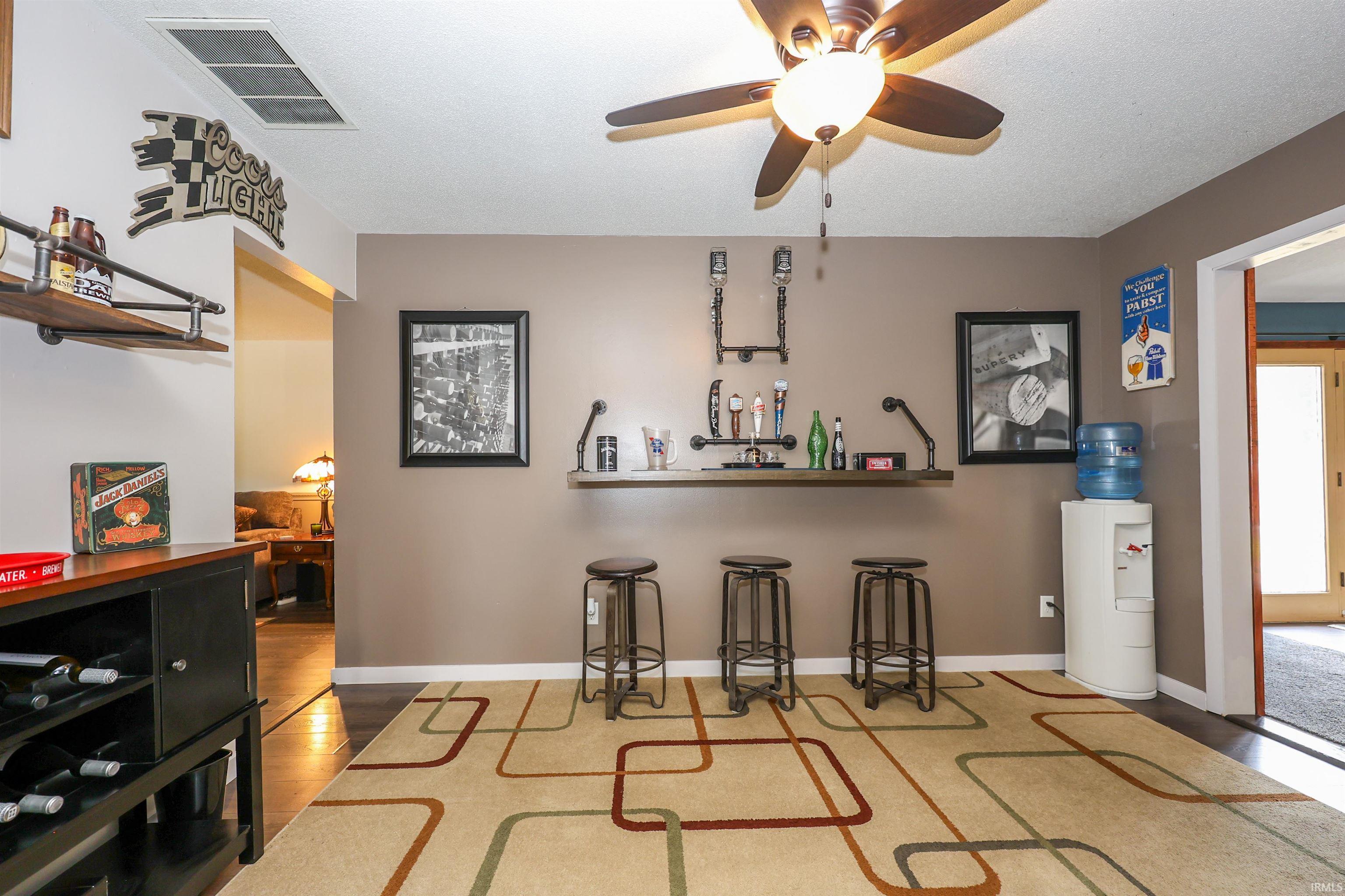 Recessed wall bar featuring a wood-finish shelf and pipe-style fixtures, complemented by dark-finish flooring and a ceiling fan with integrated lighting