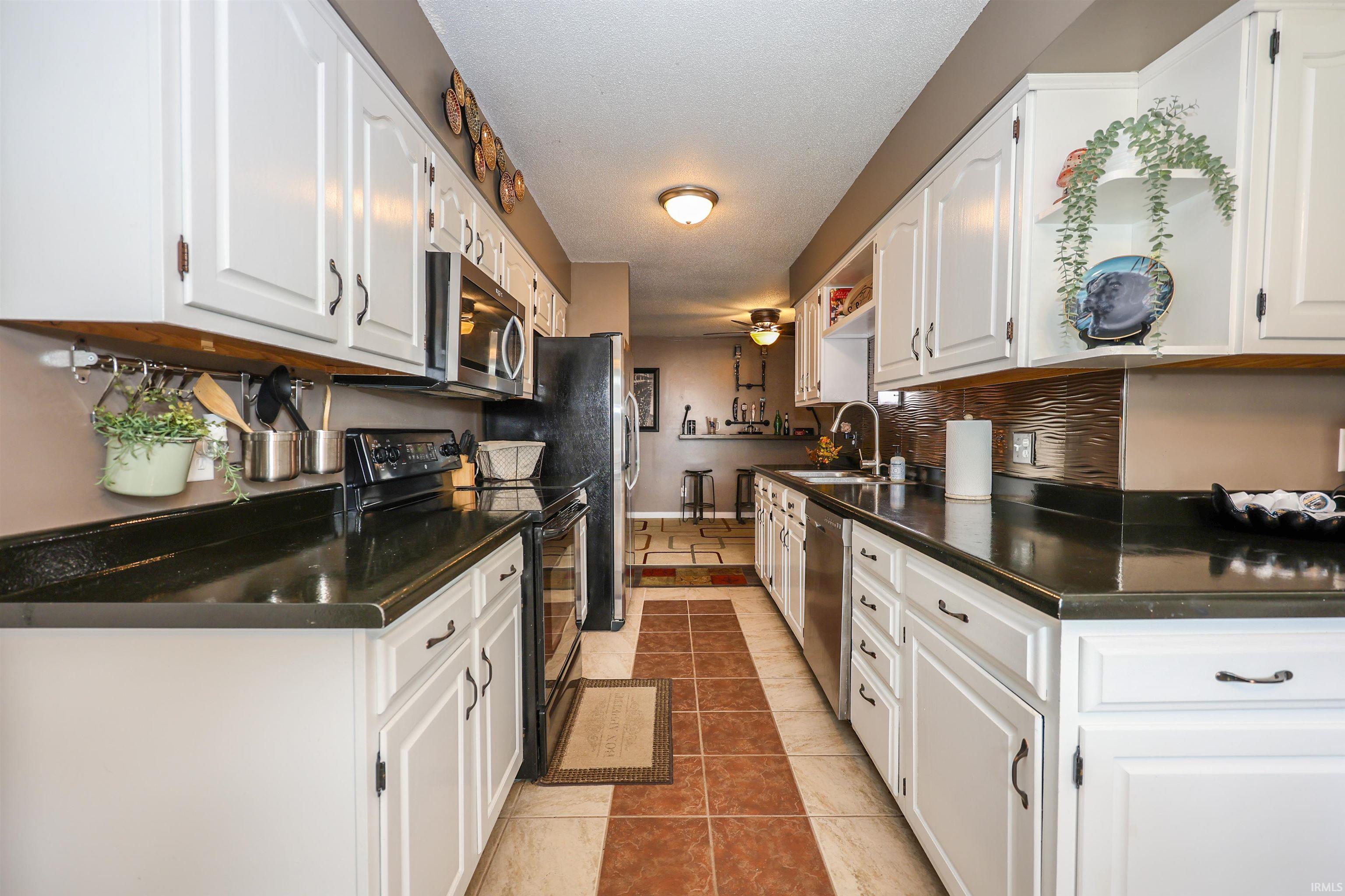 Galley kitchen featuring white cabinetry, dark countertops, a tile floor with a decorative inlay, stainless steel appliances, and a tile backsplash