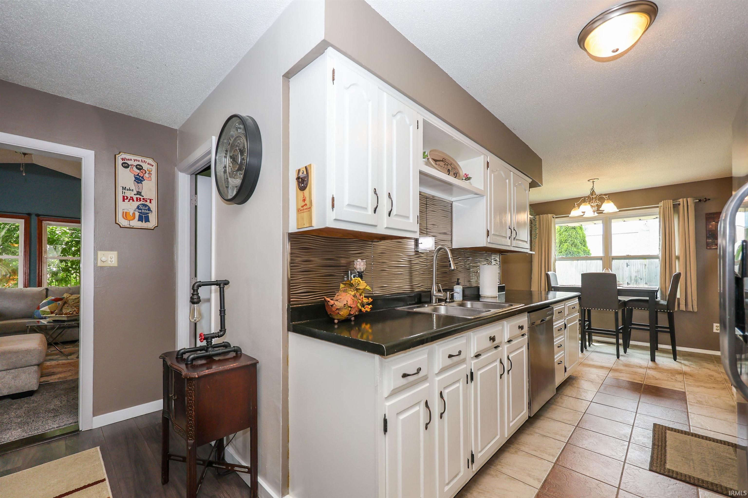 White cabinetry with dark hardware, dark countertops, and a textured tile backsplash