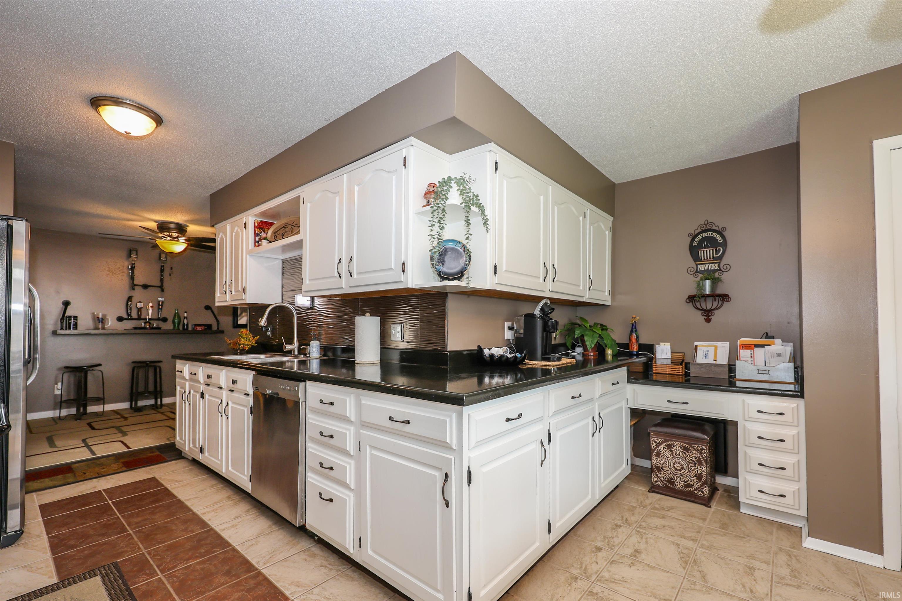 Kitchen featuring white cabinetry, dark countertops, a stainless steel dishwasher, and a metallic tile backsplash