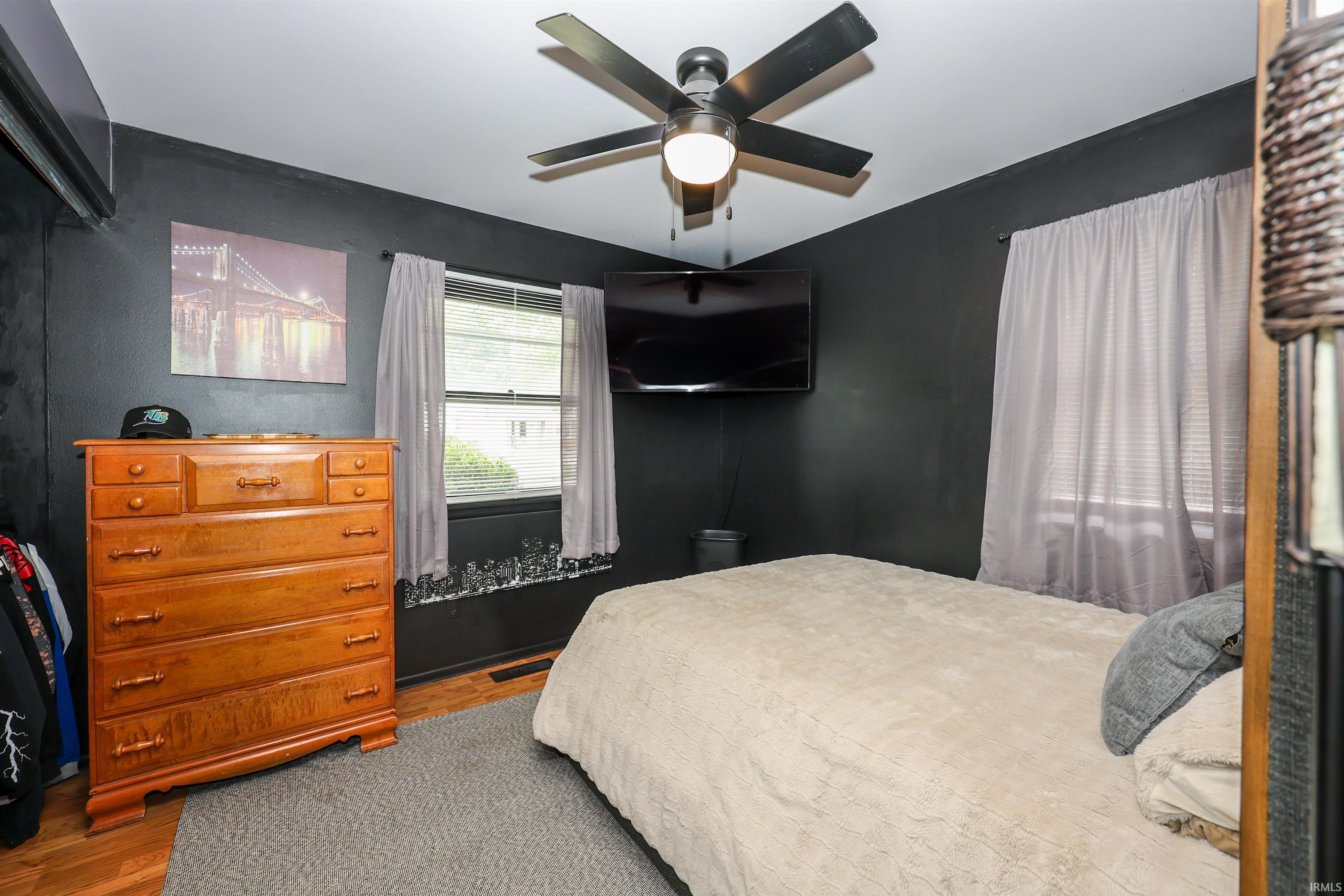 Bedroom featuring wood-finish flooring, a ceiling fan with integrated lighting, and two windows with light-filtering curtains