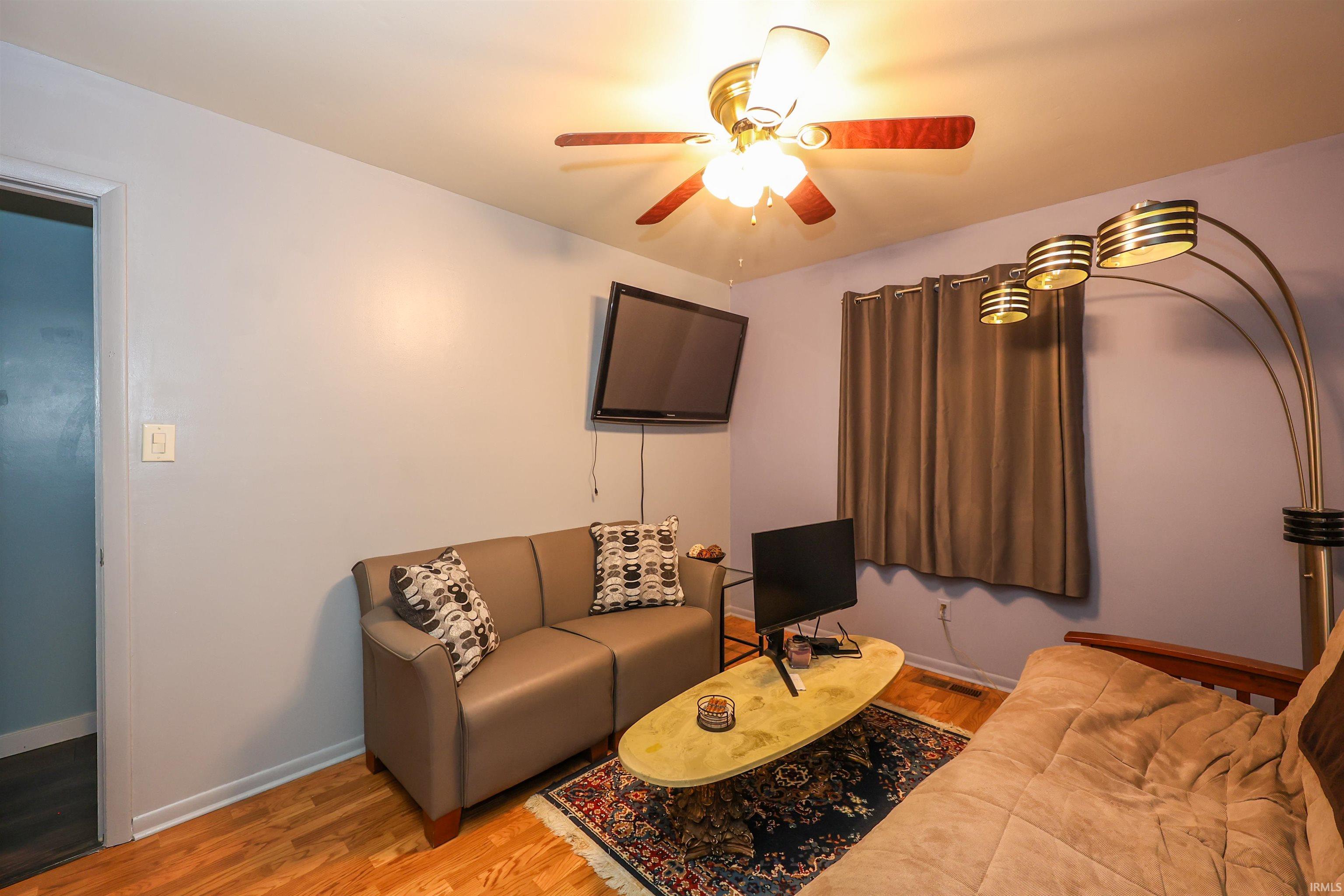 Hardwood flooring extending throughout, ceiling fan with integrated lighting, window with curtain rod and drapes, and light-toned wall paint