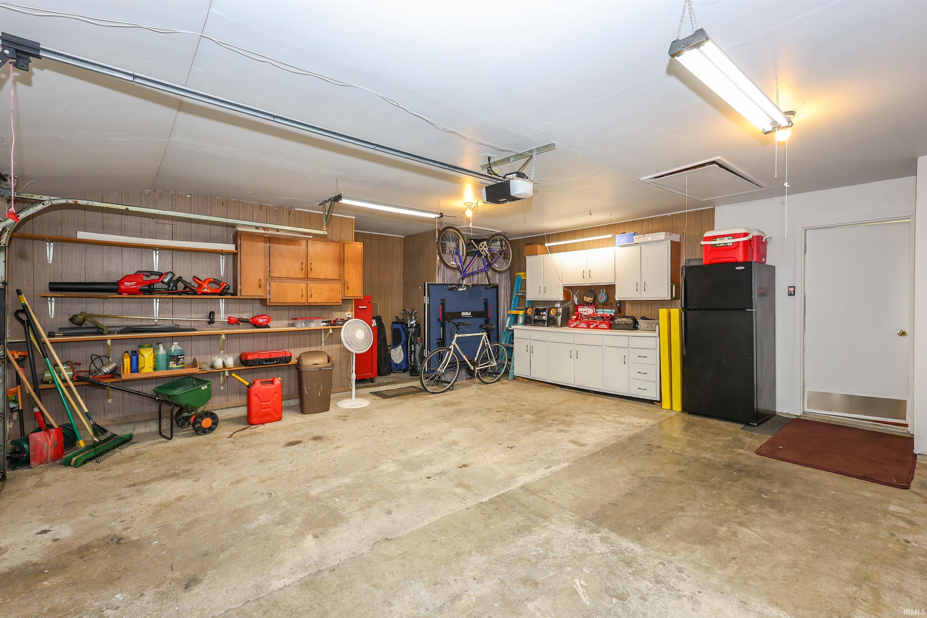 Spacious garage featuring a concrete floor, fluorescent lighting, built-in shelving, and white cabinetry with a countertop