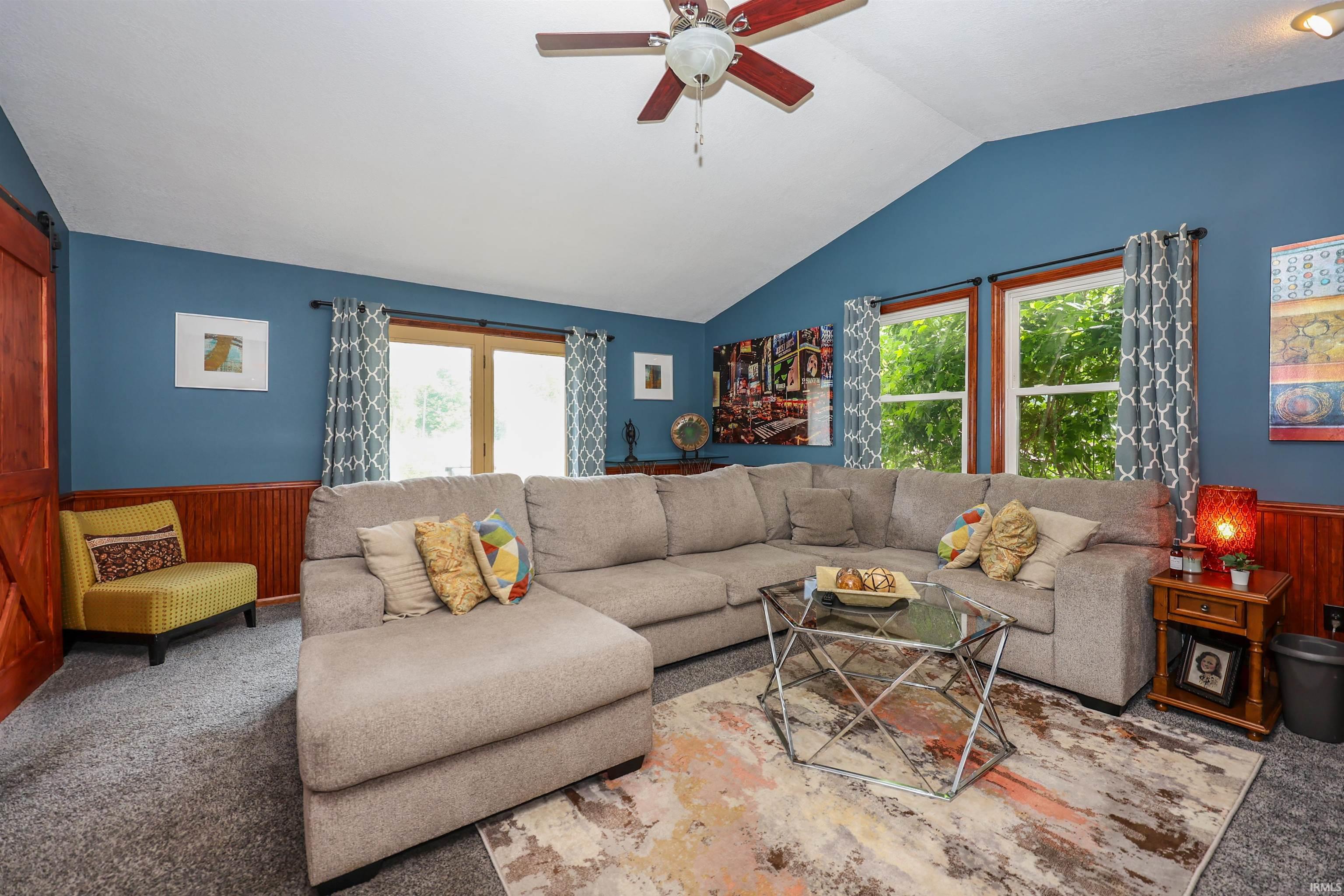 Spacious room featuring vaulted ceilings, a ceiling fan, and wood-paneled wainscoting