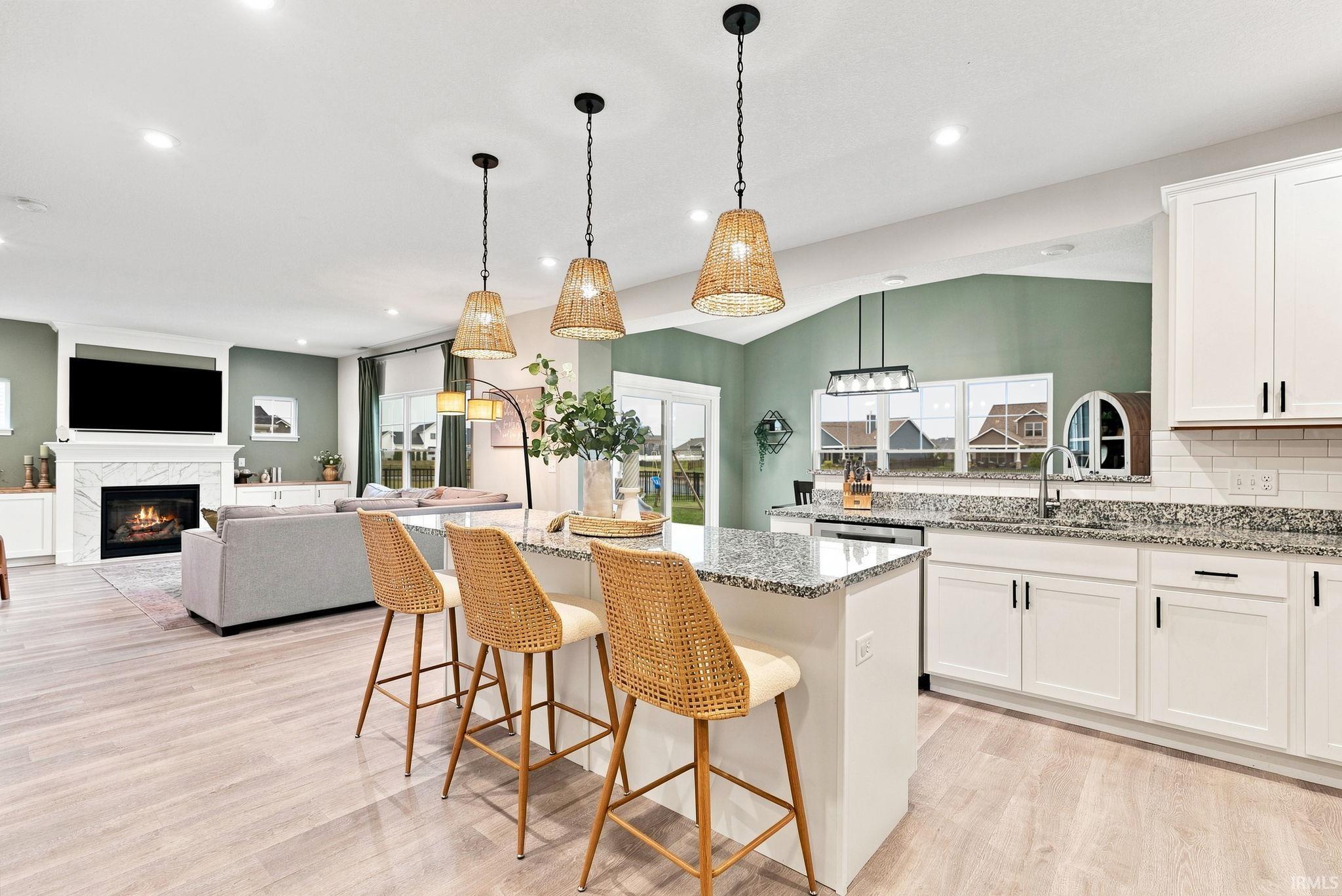 Open-concept living space featuring a central kitchen island with seating, pendant lighting, wood-finish flooring, a contemporary fireplace, and white cabinetry