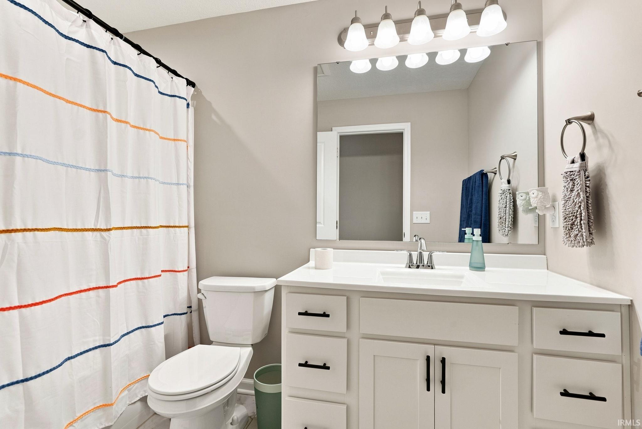 Bathroom featuring a vanity with white cabinetry, a single basin sink, and a large mirror with overhead lighting