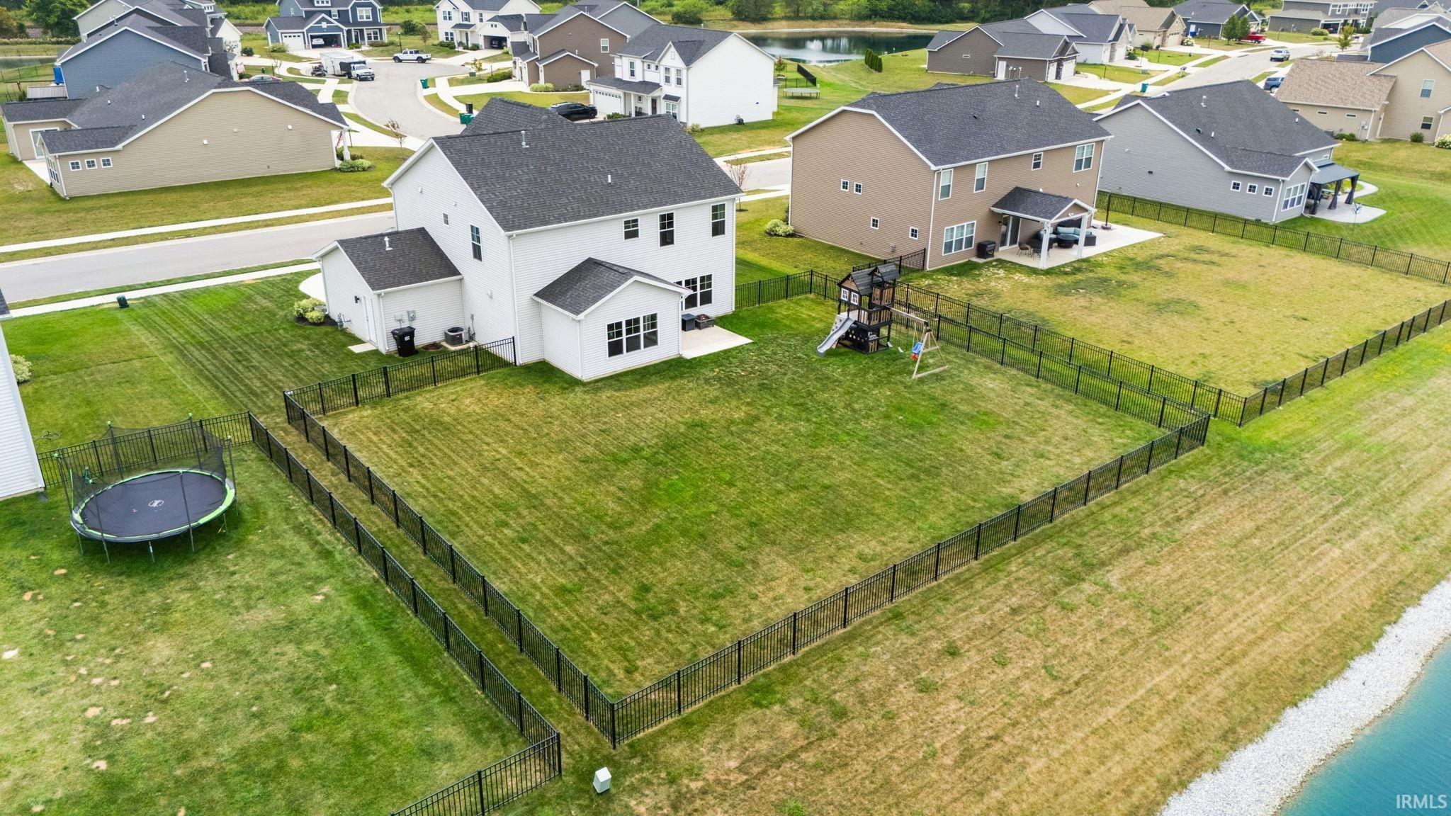 Expansive fenced backyard featuring a two-story residence with a dark roof and a paved patio area