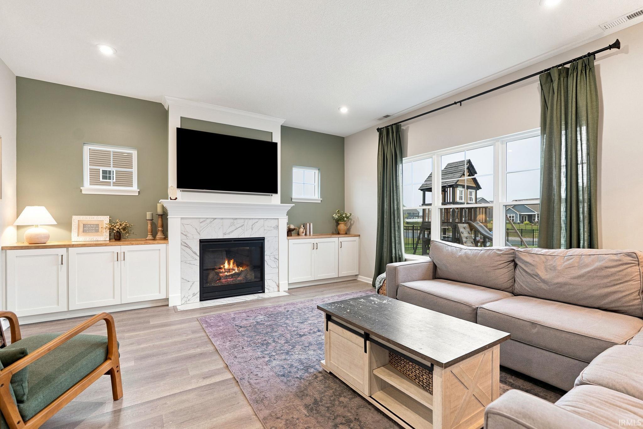 Living area featuring a fireplace with marble-look surround, custom built-in cabinetry with wood-finish countertops, recessed lighting, and large windows with privacy curtains