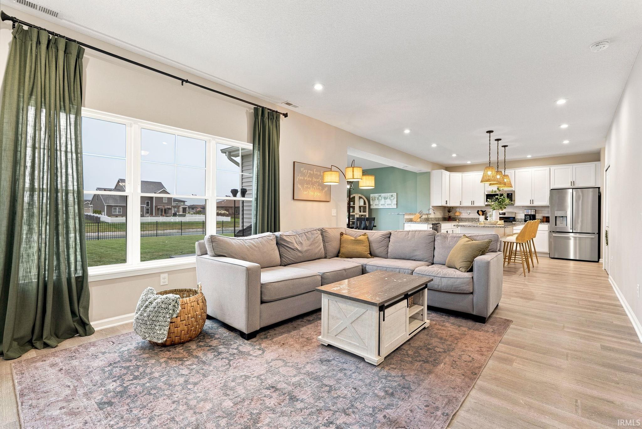 Open-concept living space featuring wood-finish flooring, a large multi-pane window, recessed lighting, a kitchen with white cabinetry, and stainless steel appliances