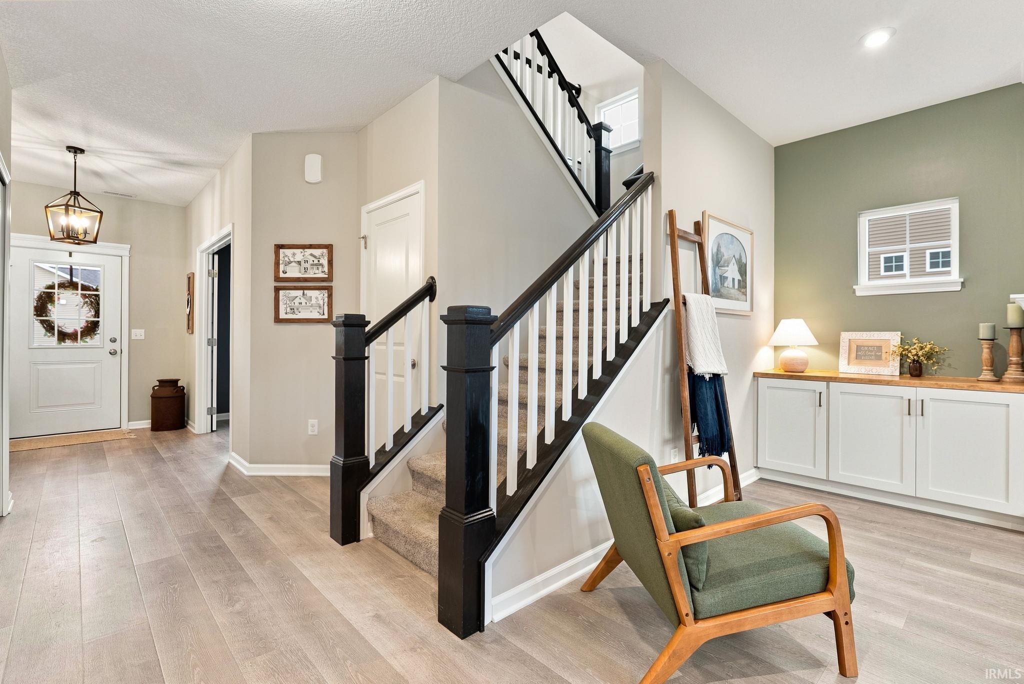 Foyer featuring light wood-finish flooring, a contemporary staircase with dark newel posts and handrails, and a built-in cabinet system with a wood countertop