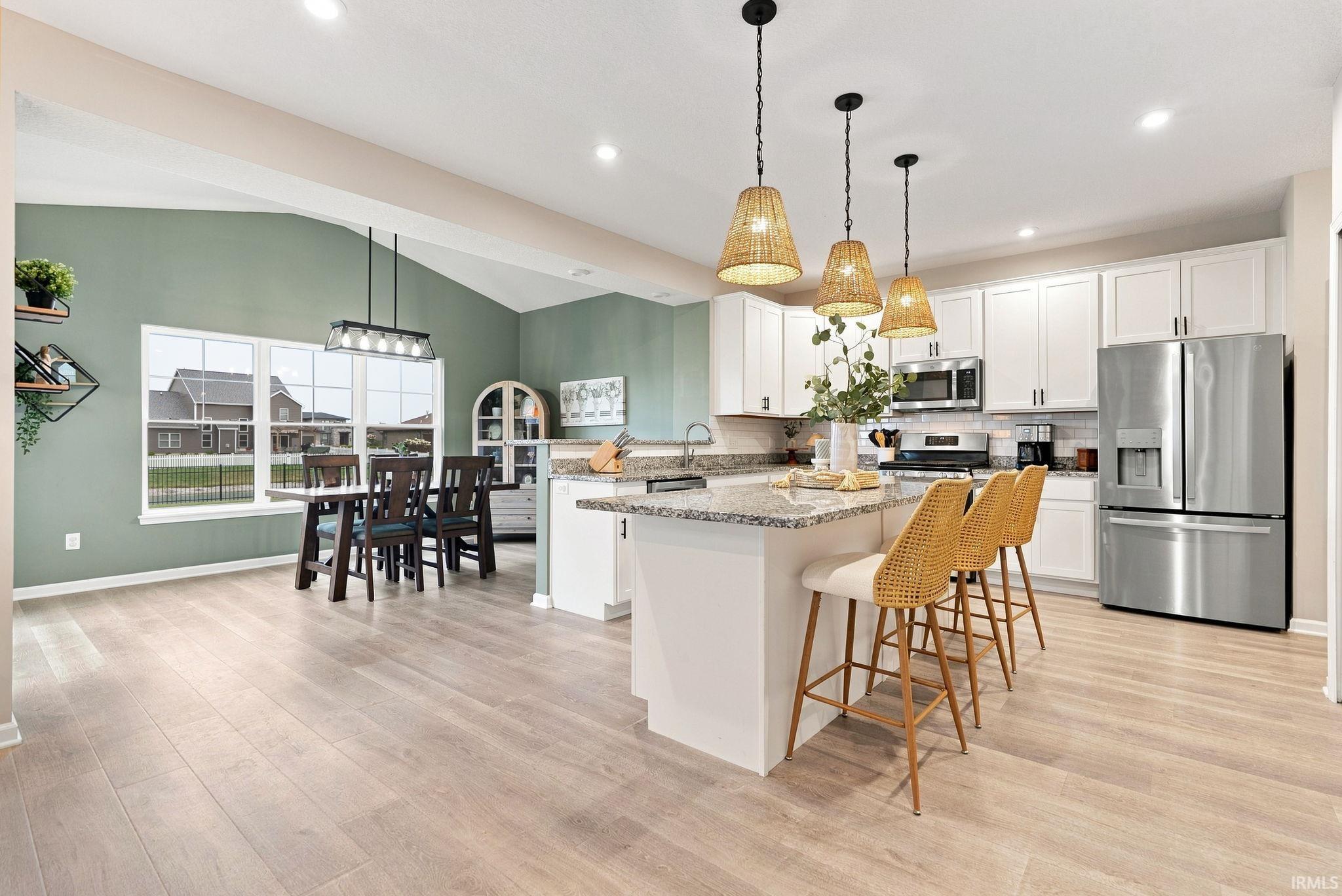 Open-concept kitchen and dining area featuring light wood-finish flooring, a vaulted ceiling, and recessed lighting