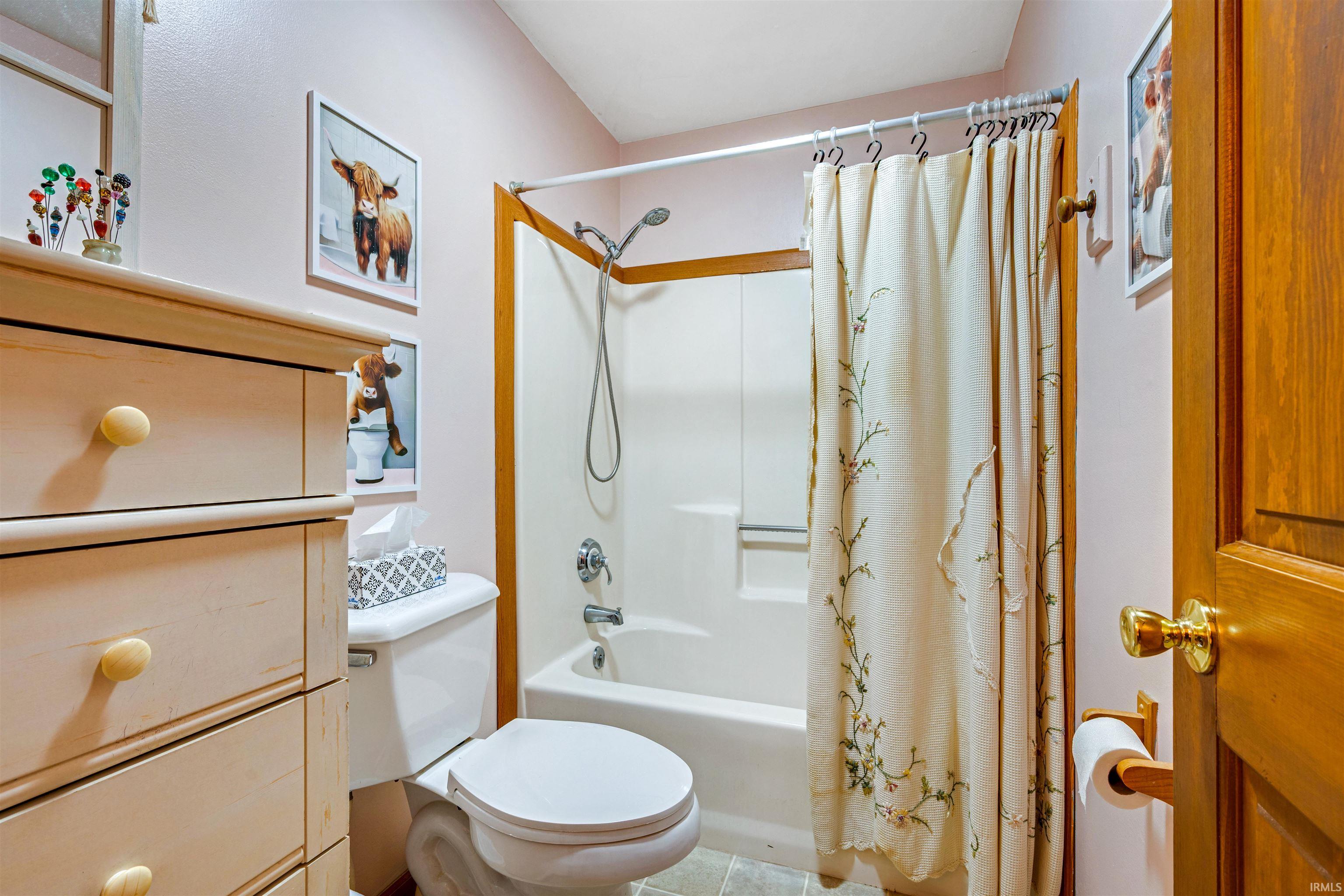 Bathroom featuring a complete tub and shower unit, a commode, and warm-toned wood-finish flooring