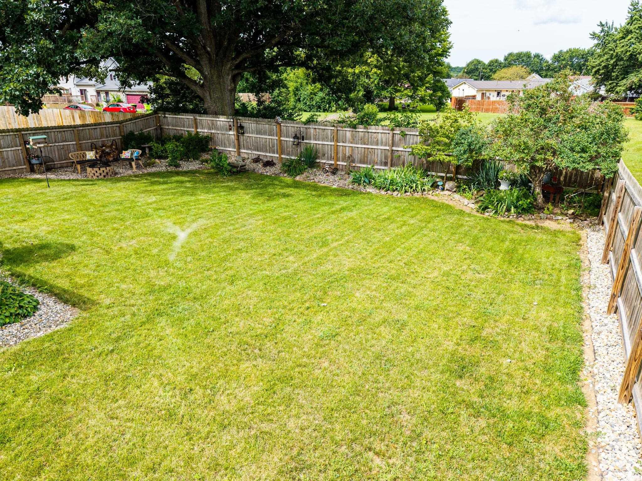 Expansive backyard featuring a lush lawn, perimeter wood fencing, and mature trees