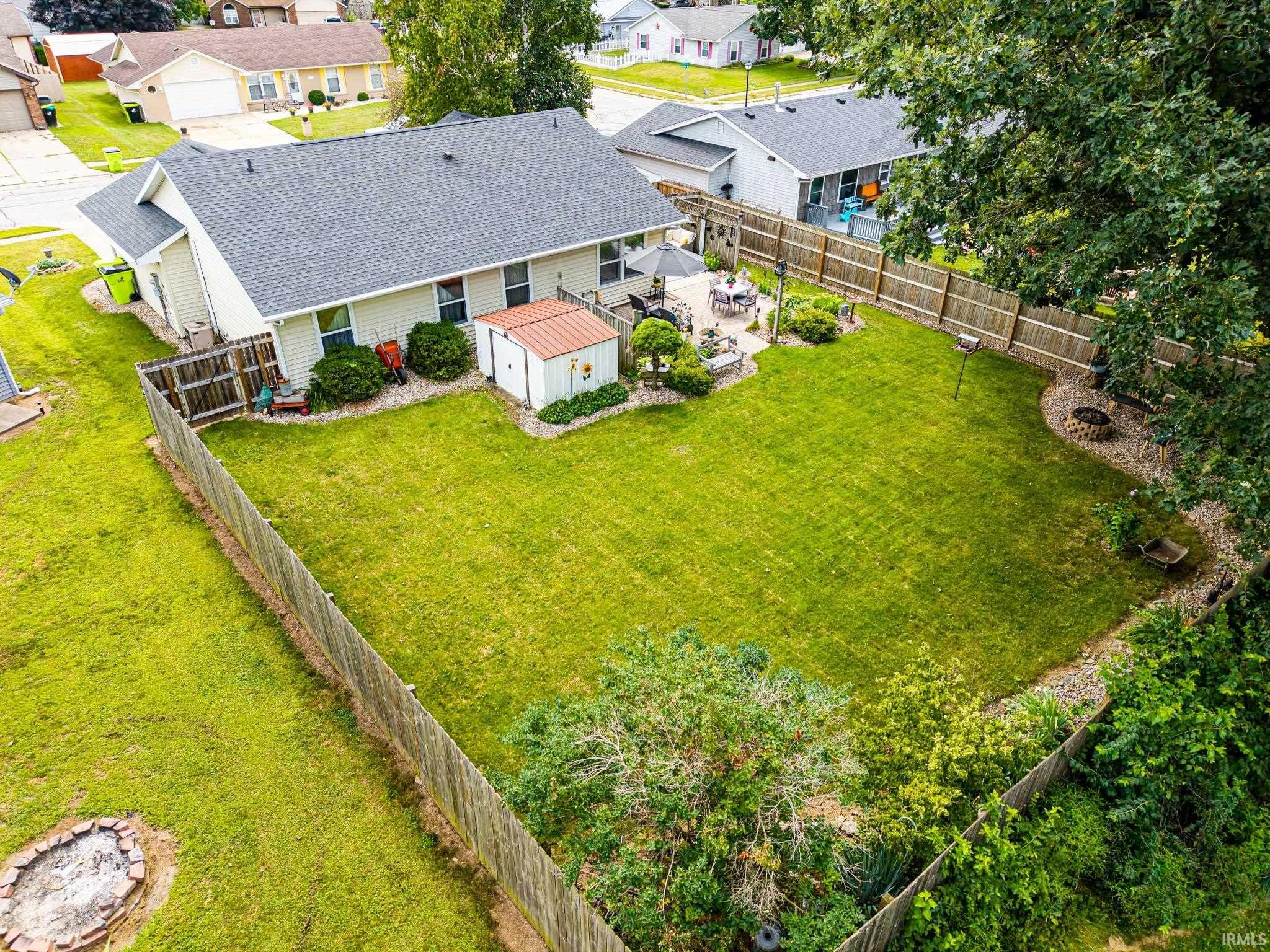 Expansive backyard featuring a manicured lawn, a privacy fence, a concrete patio, a storage shed, and mature perimeter landscaping