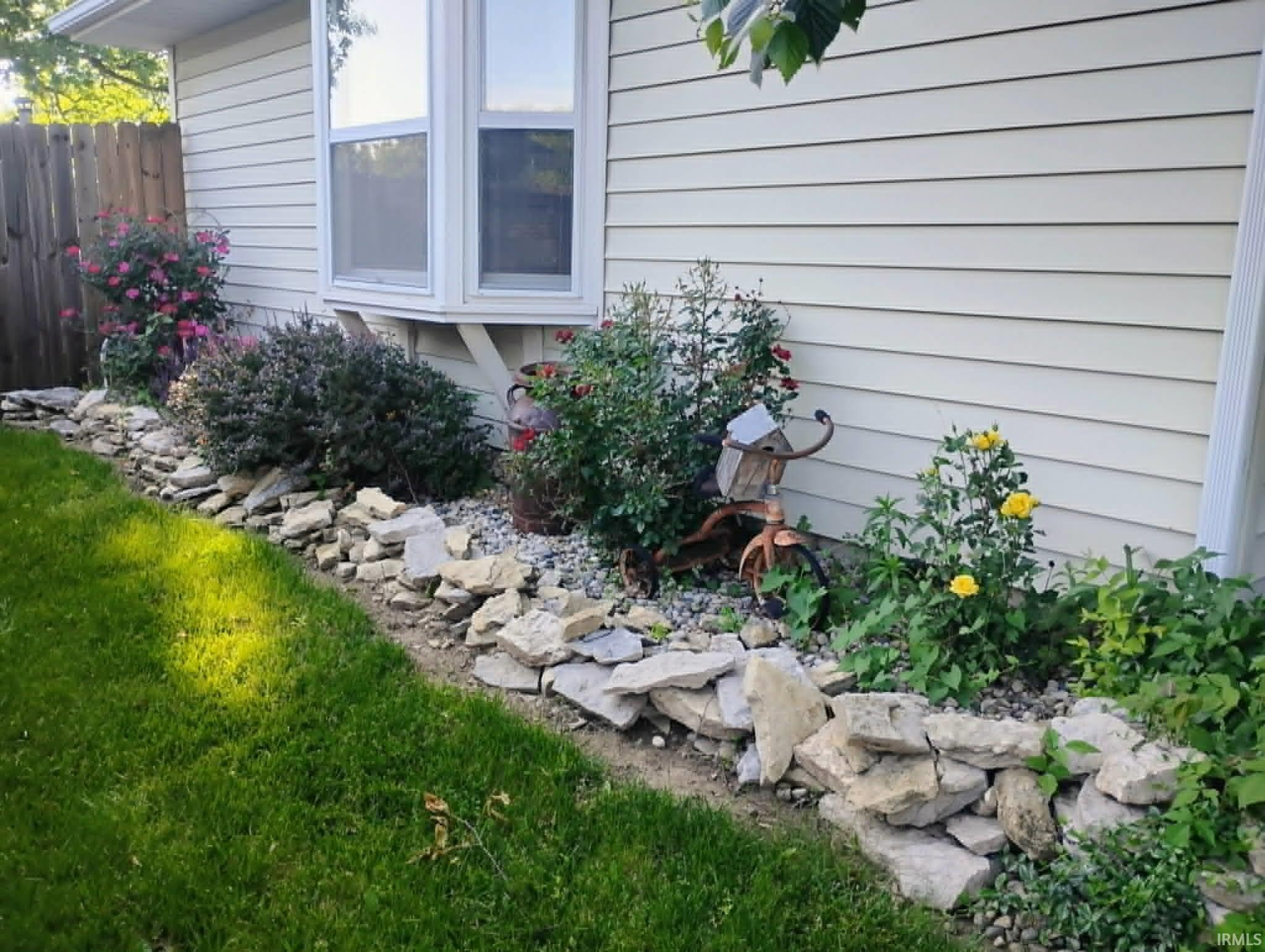 Landscaped border featuring a stone retaining wall, mature shrubs, and flowering plants