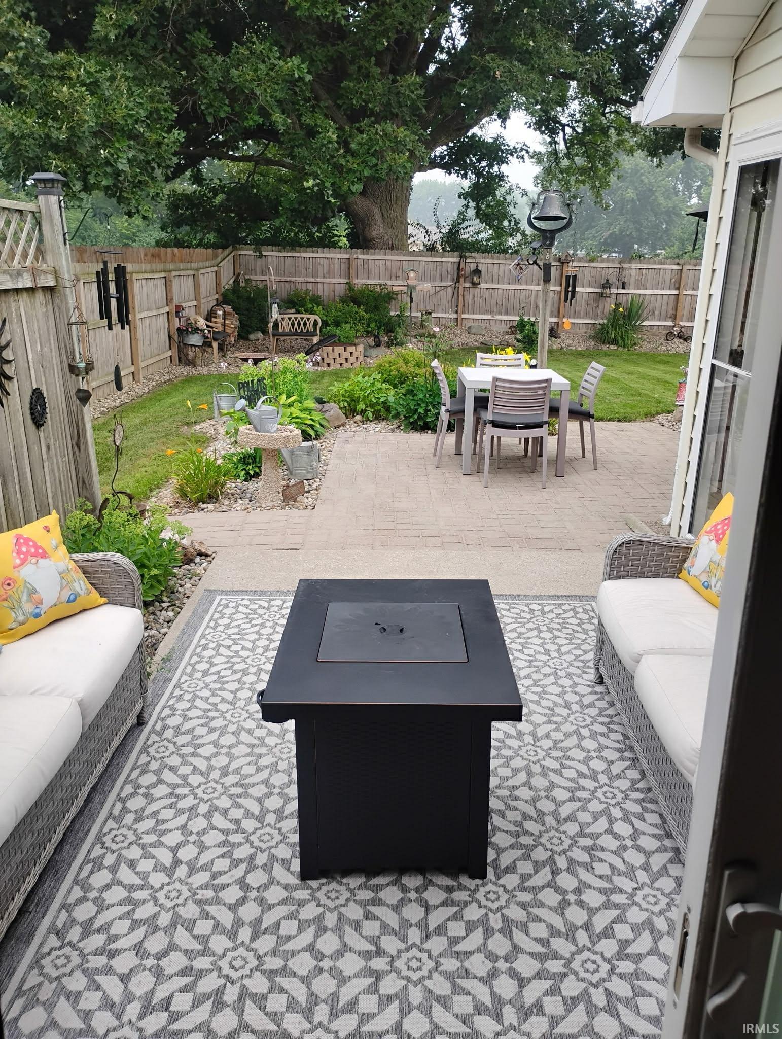 Paved patio featuring a built-in fire pit, two wicker sofas, and a geometric pattern outdoor rug