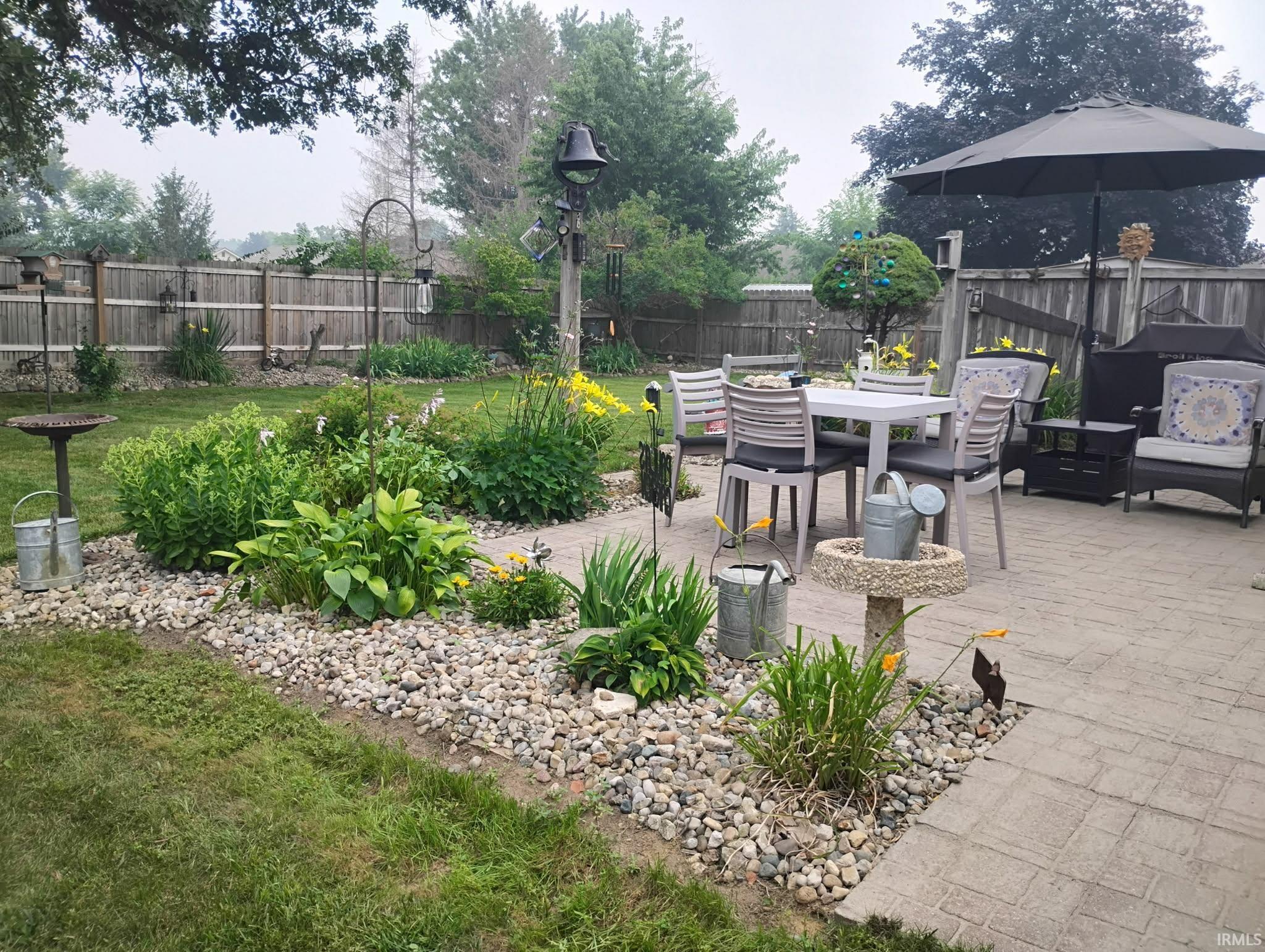 Expansive backyard featuring a stone paver patio, a landscaped garden bed with river rock accents, a manicured lawn, and a wood privacy fence