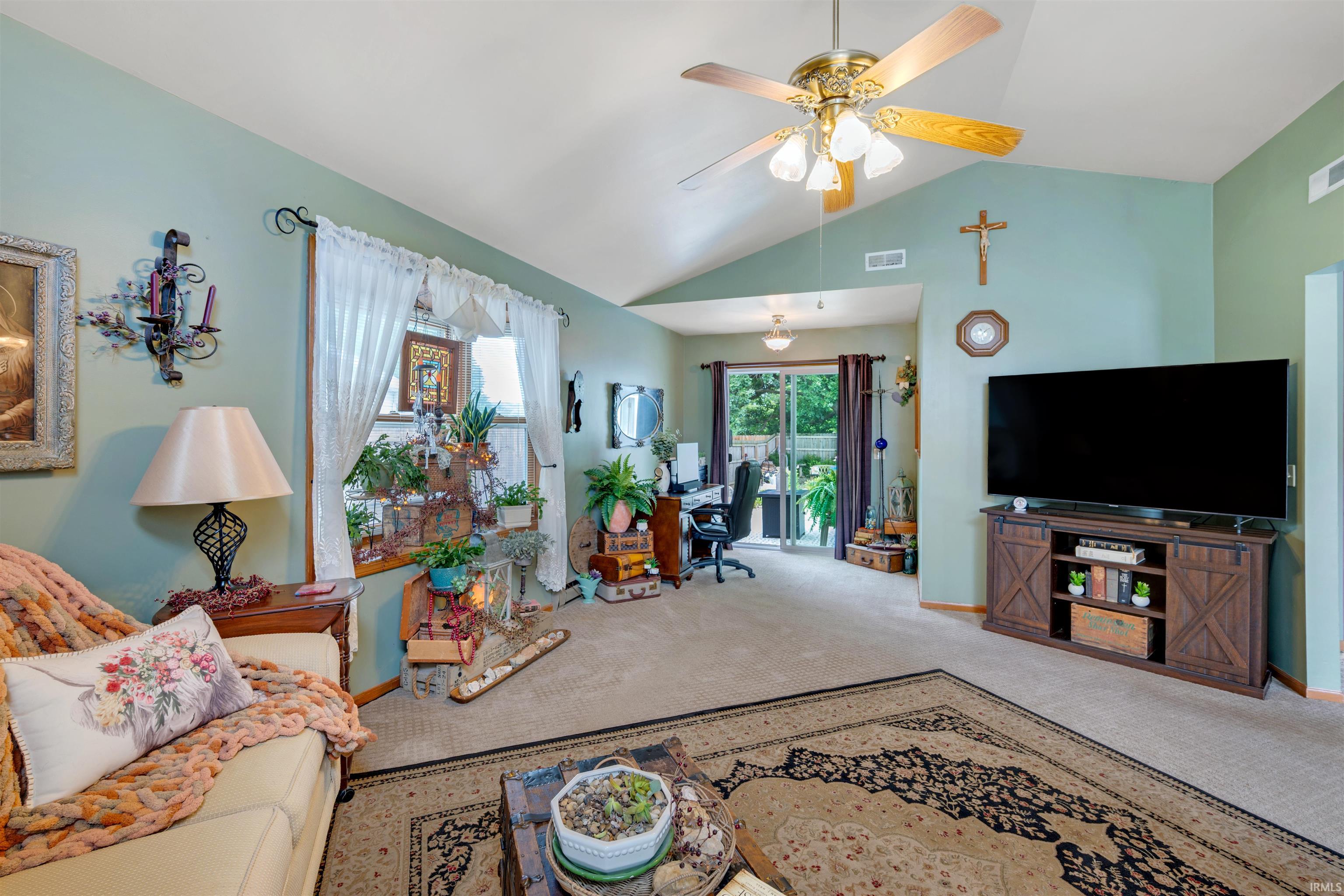 Vaulted ceiling living area featuring a ceiling fan with integrated lighting, wood-finish flooring, and a sliding glass door leading to the exterior