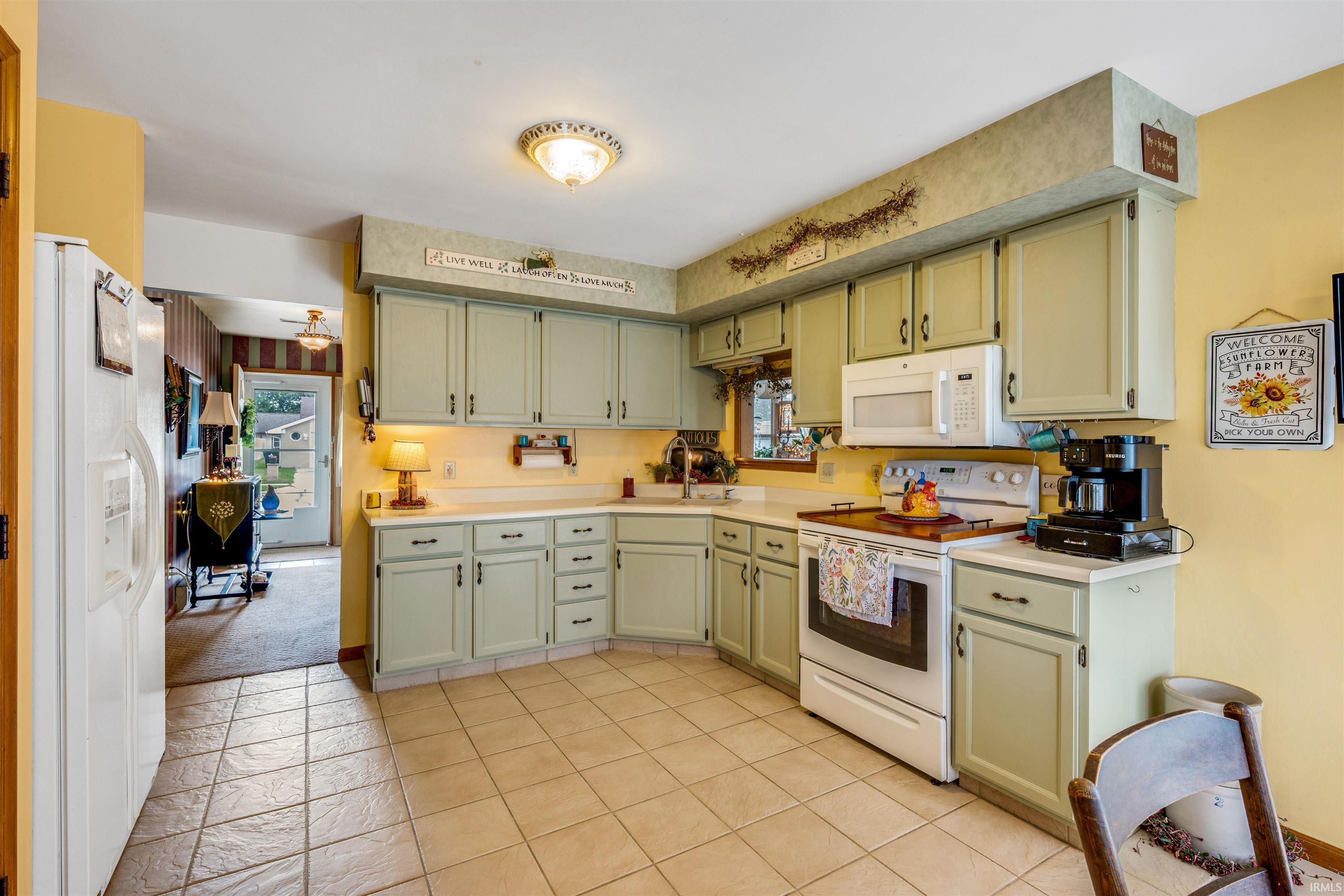 Kitchen featuring light green cabinetry, white appliances, and a tiled floor