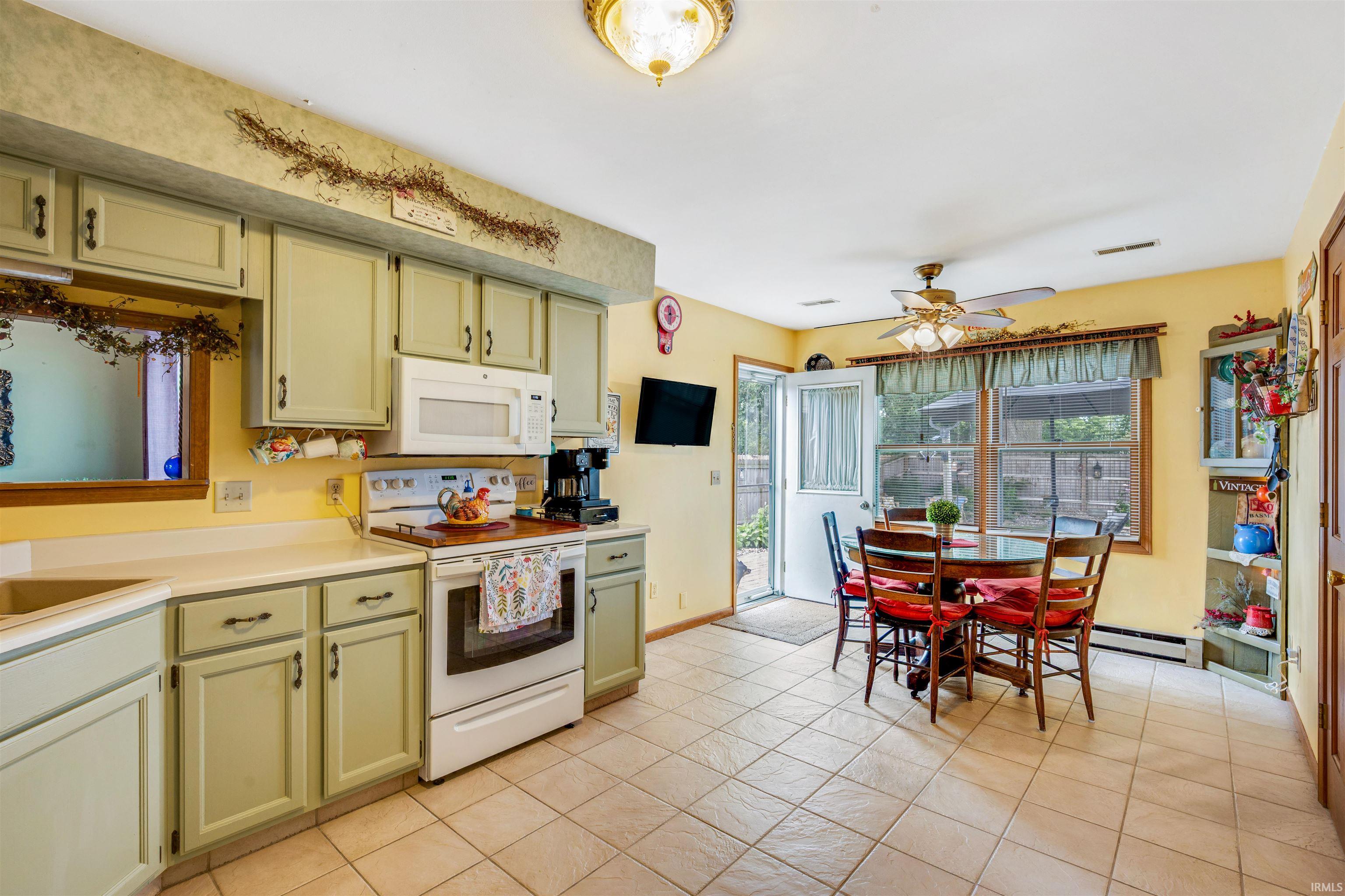 Kitchen featuring light green cabinetry, white appliances, and light-toned tile flooring