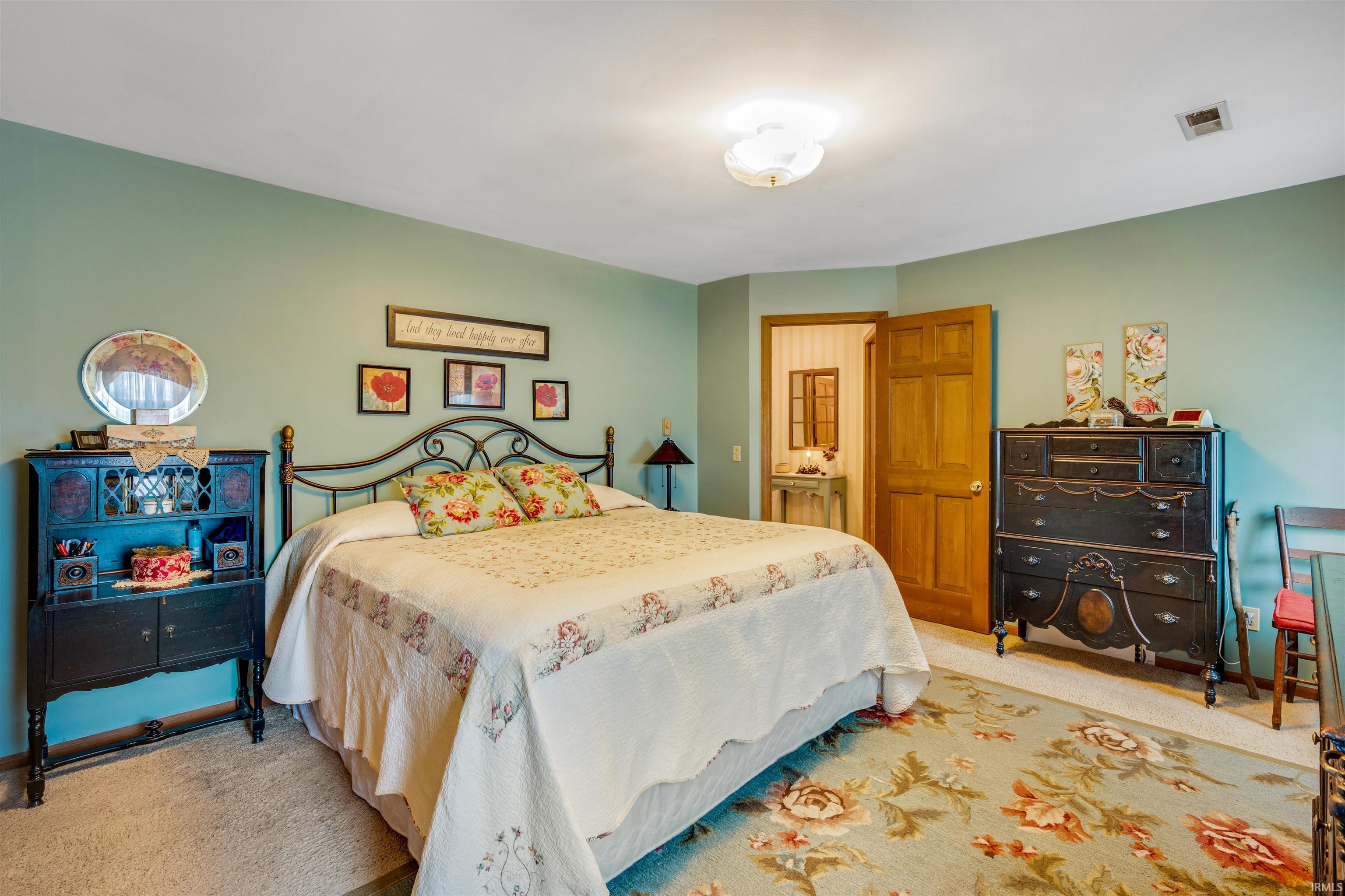Spacious room featuring light teal wall paint, carpet flooring, a natural wood door, and a flush mount ceiling light fixture