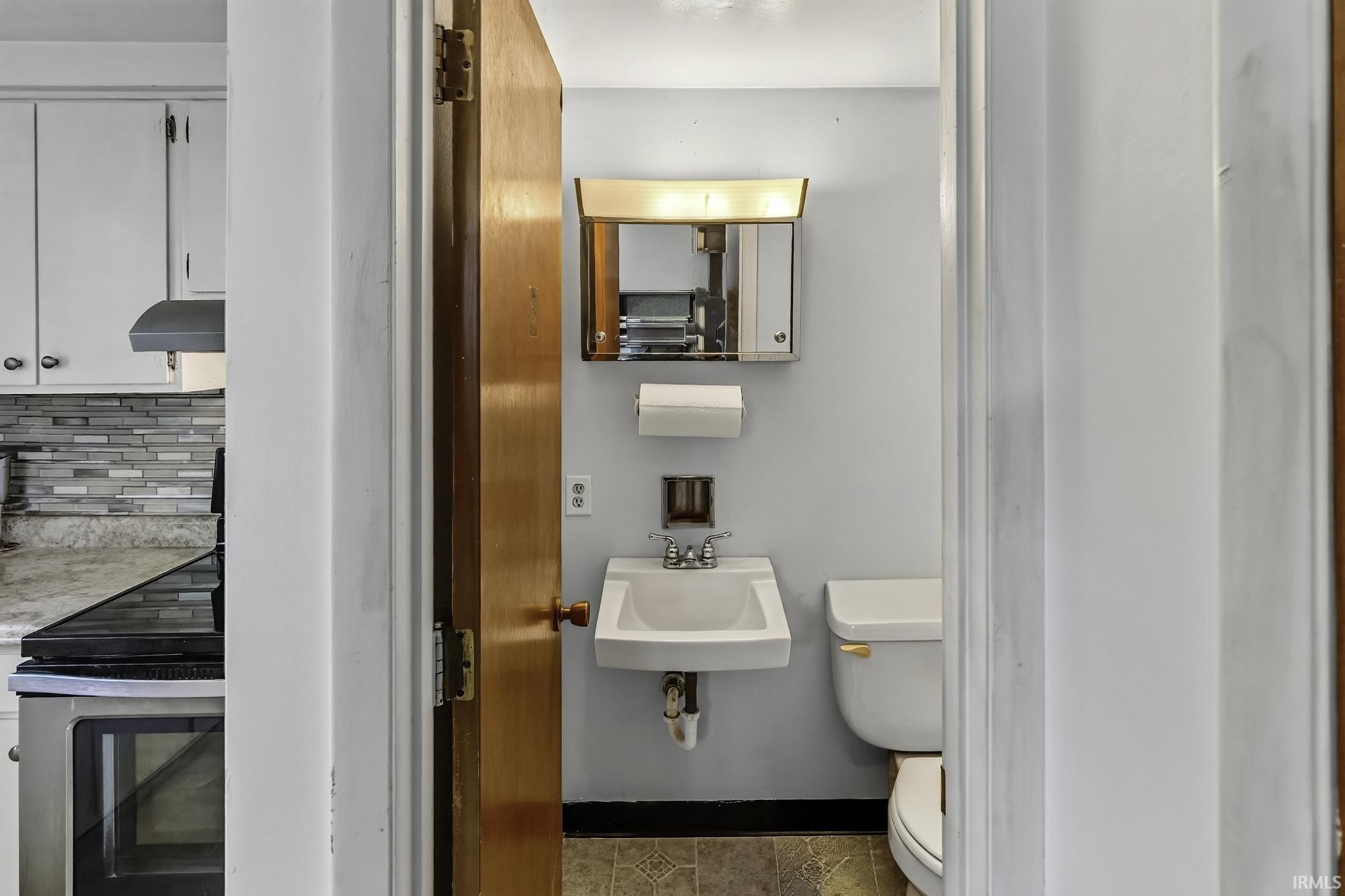 Compact bathroom featuring a wall-mounted sink, toilet, and mirrored medicine cabinet