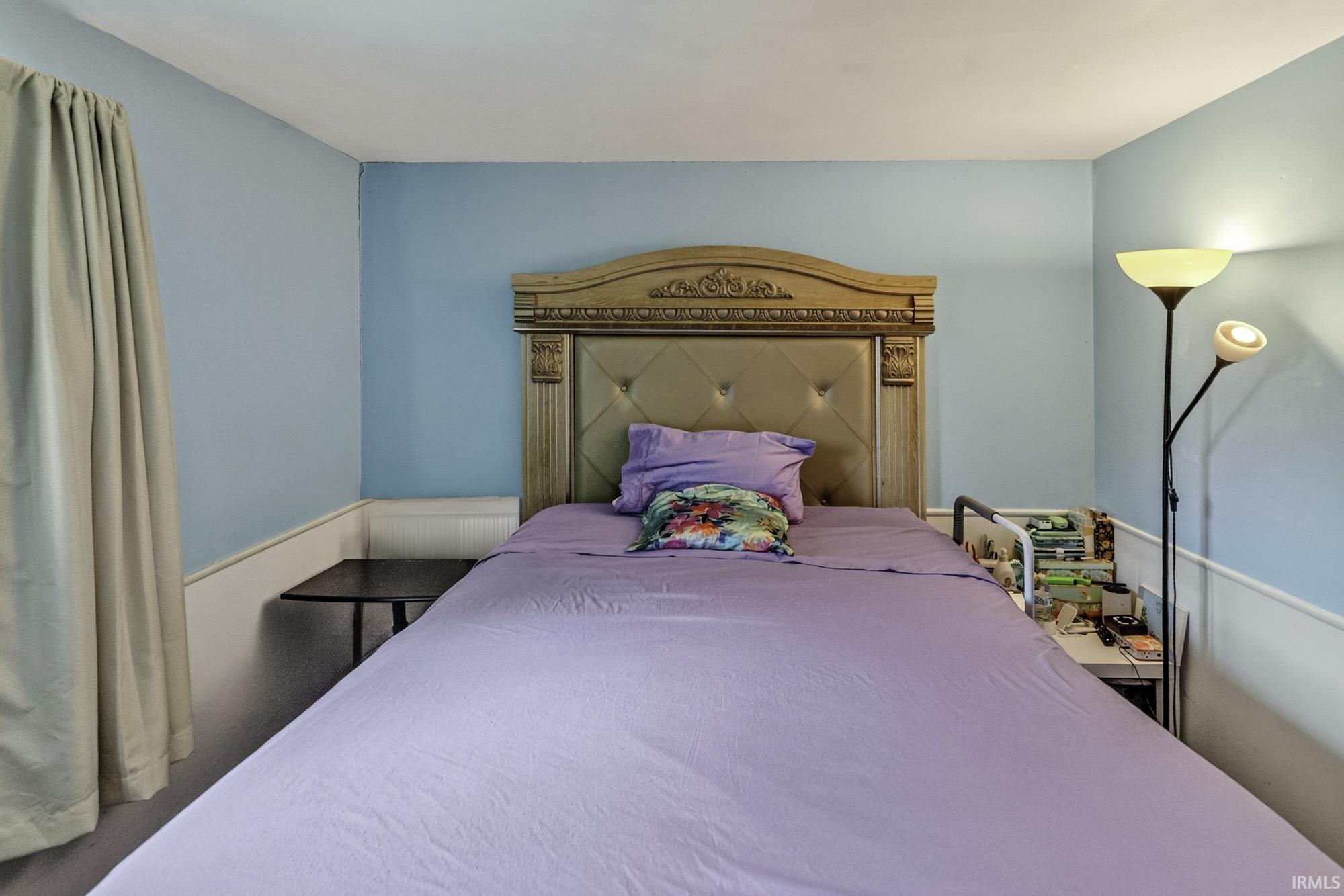 Bedroom featuring light blue walls, white wainscoting, and a window with neutral drapes