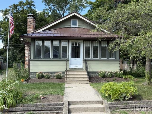 Cottage-style residence featuring a metal roof, brick chimney, and light green siding