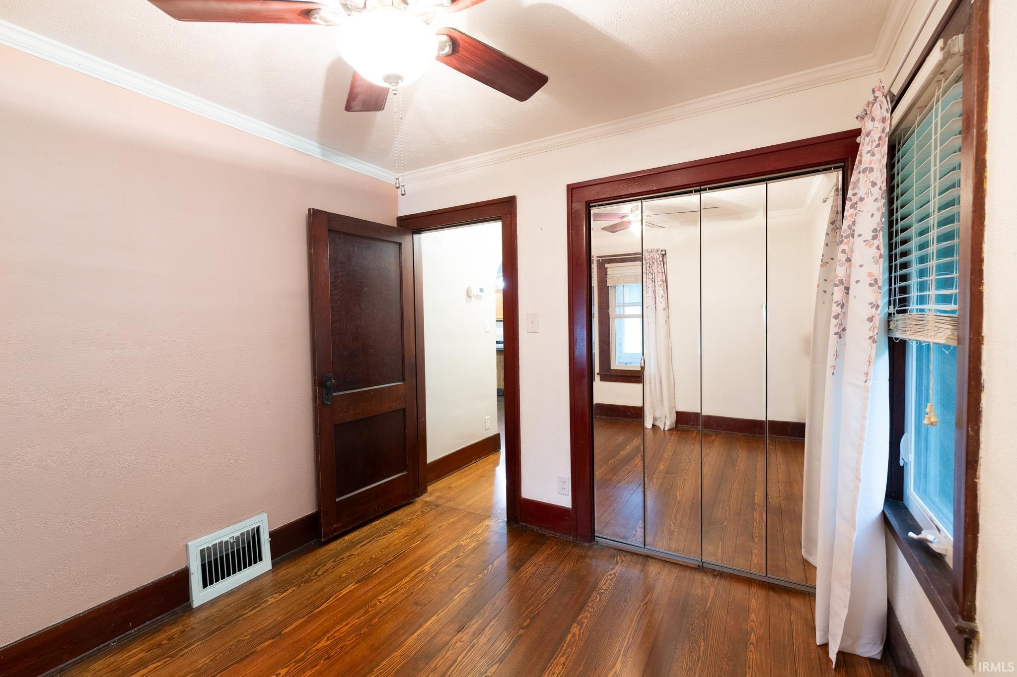 Hardwood flooring throughout, featuring a ceiling fan with integrated lighting, mirrored closet doors, a built-in window, and dark wood trim