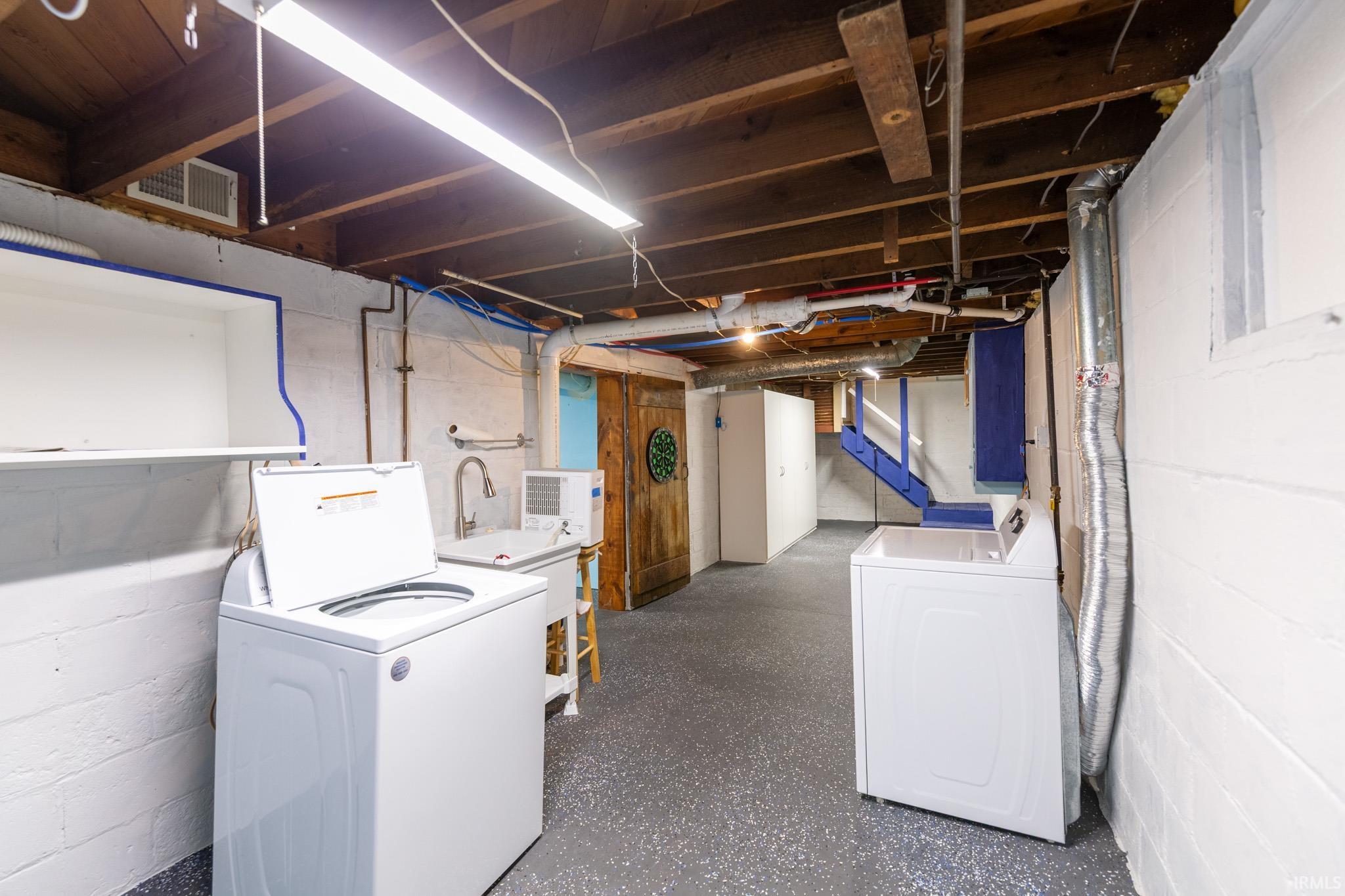 Spacious utility room featuring exposed wood ceiling joists, durable painted concrete block walls, and a utility sink with a gooseneck faucet