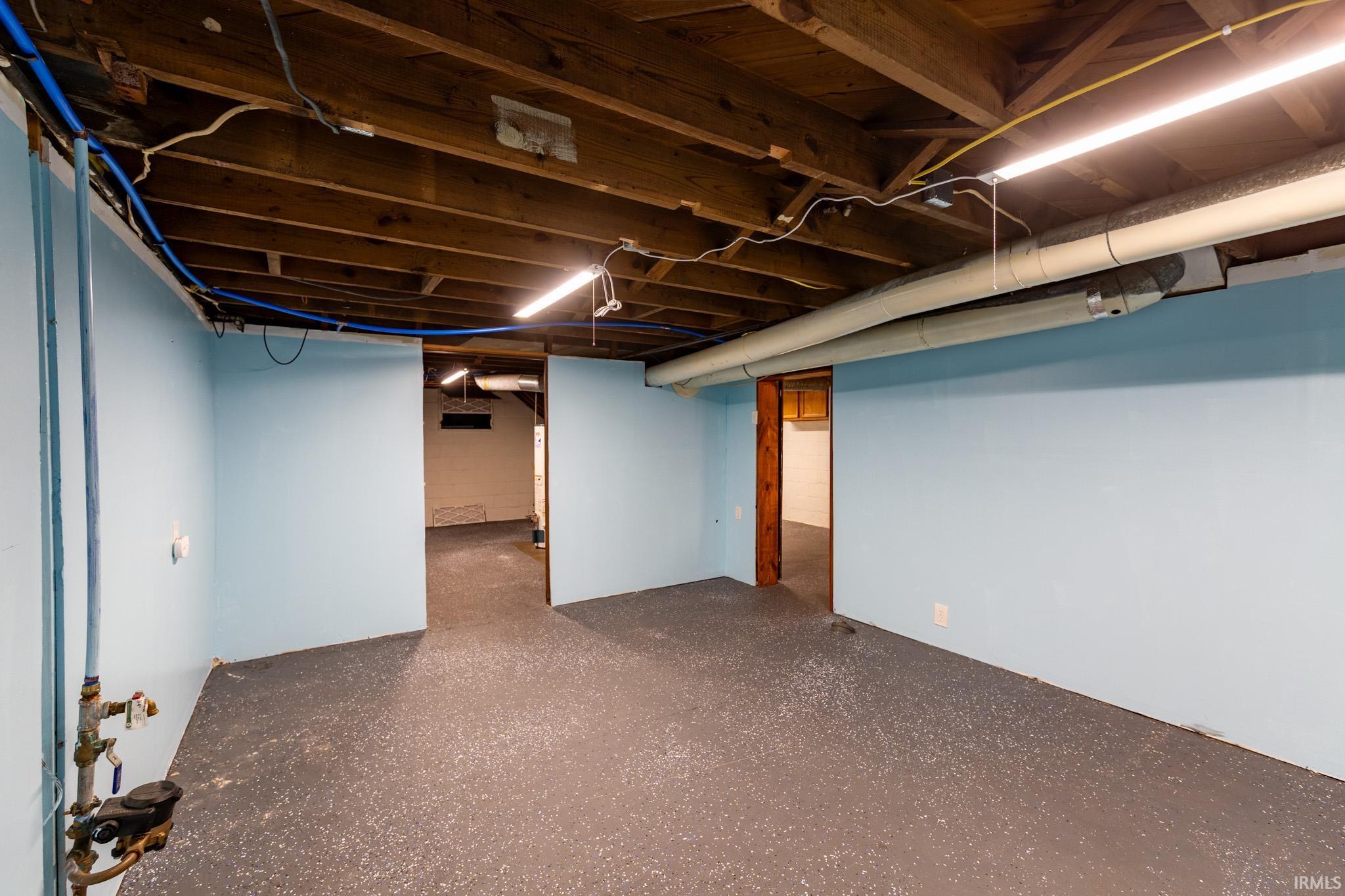 Unfinished basement featuring exposed wood ceiling joists, light blue painted walls, and a gray floor